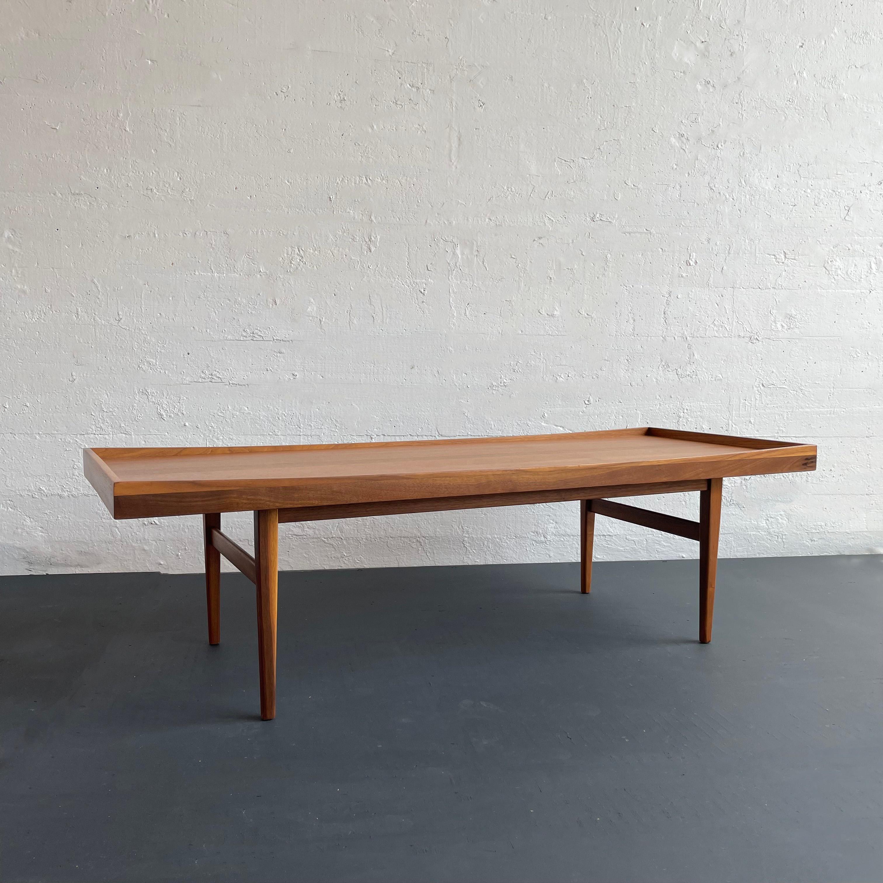 Classic, mid-century modern, walnut coffee table designed by Kipp Stewart & Stewart MacDougal for American Design Foundation Group, Calvin Furniture features a tray top with lipped edge and beautiful natural walnut grain. The tapered legs and cross