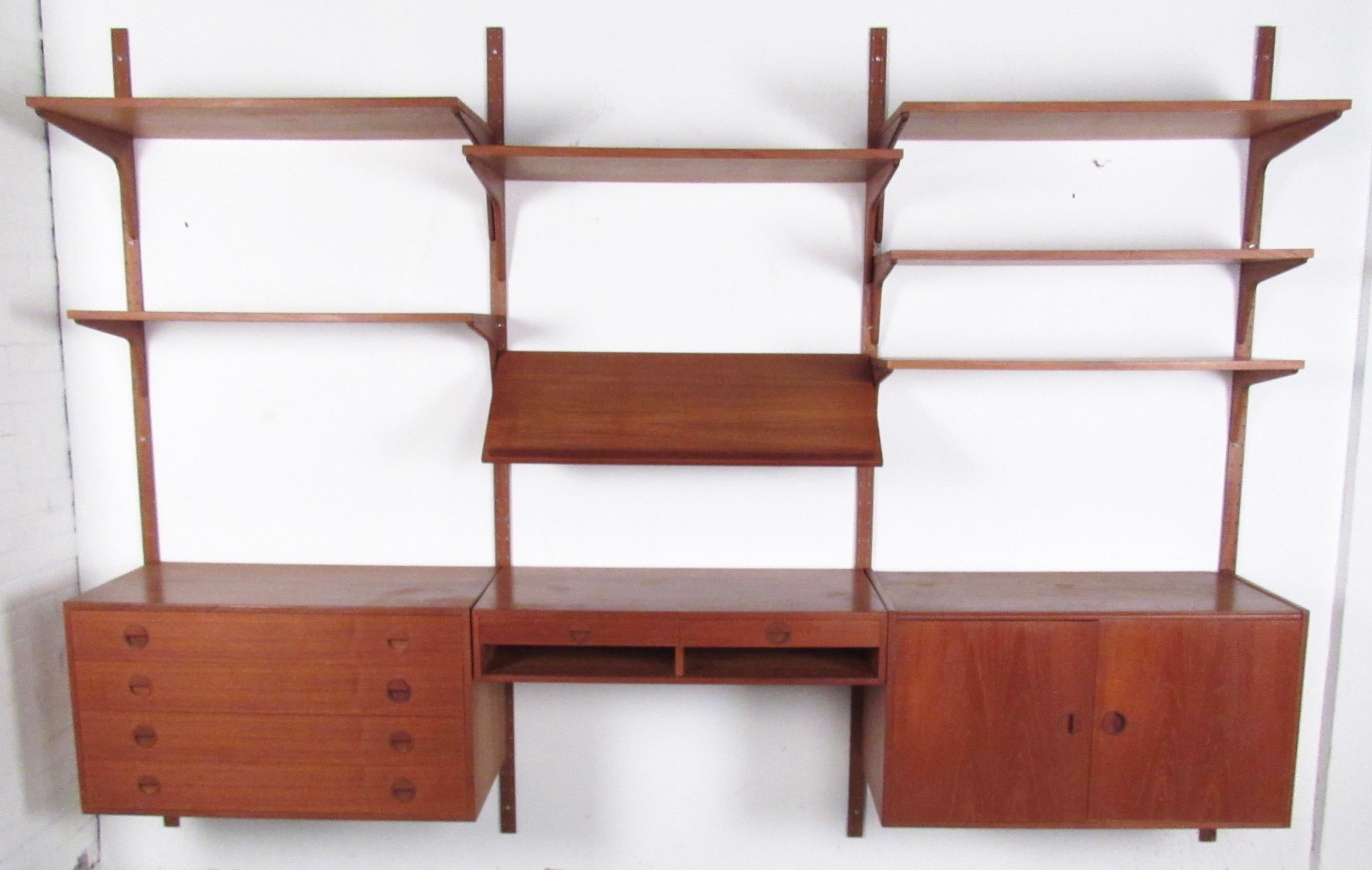 This stylish modular wall unit features midcentury teak construction and is easily arranged for optimal storage and display in any setting. Poul Cadovius style, this vintage wall-mounted bookshelf includes space for shelf storage, record cabinet,