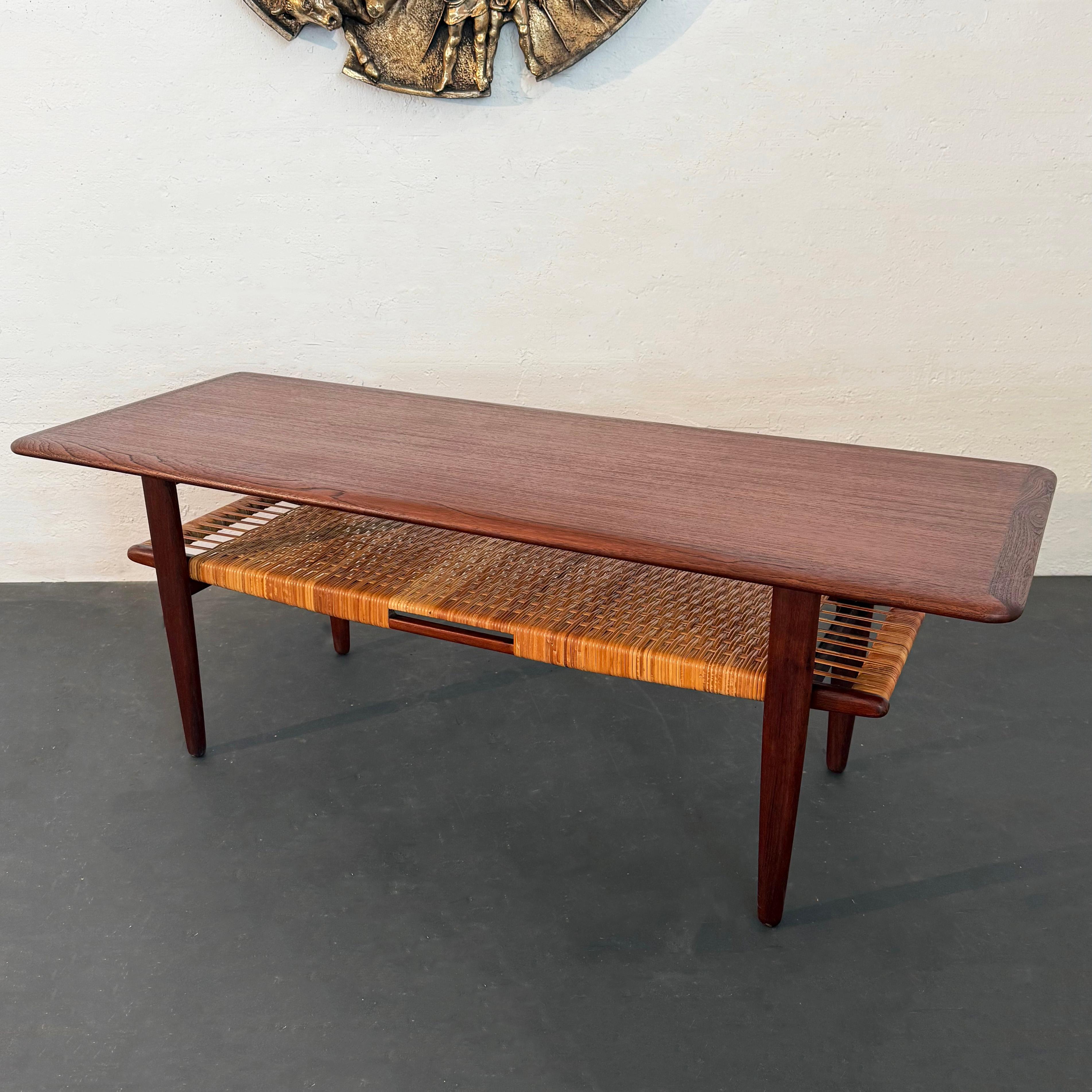 Lovely Scandinavian modern teak coffee table by Danish designer Kurt Østervig for Jason Mobler. This tiered coffee table features a rectangular top with contrasting trim and a lower caned shelf for books, magazines, remotes, etc. The frame and