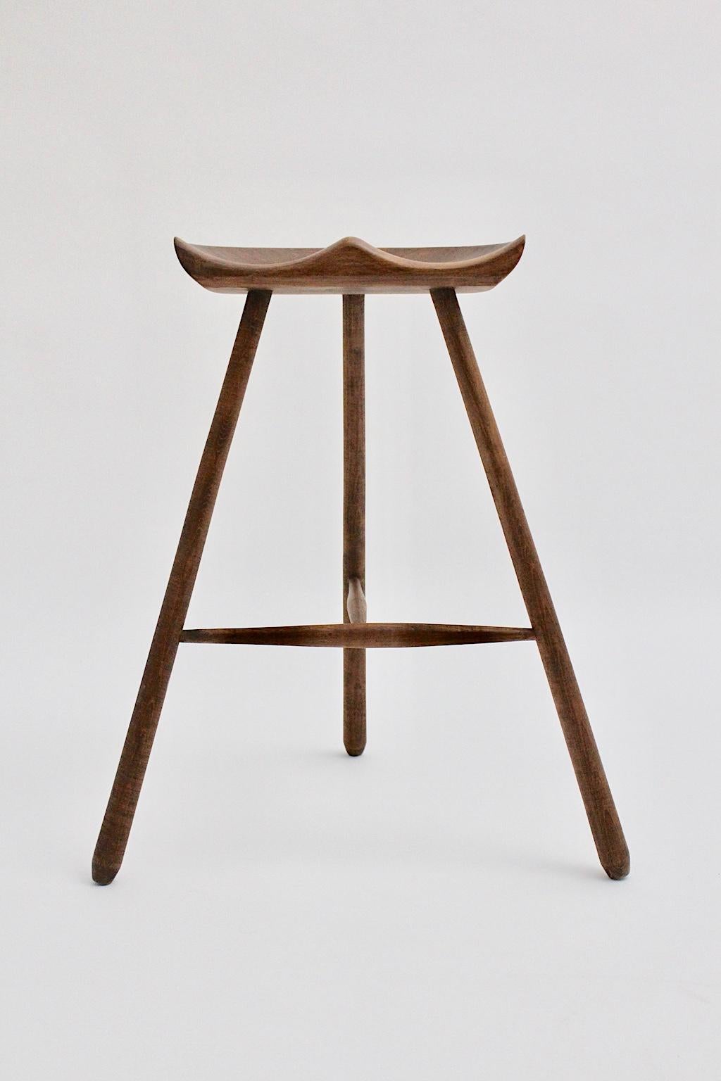 Skandinavisch-moderner dreibeiniger Teakholzhocker aus massivem Teakholz, entworfen von Arne Hovmand-Olsen in den 1960er Jahren, hergestellt in Dänemark. Drei gespreizte Füße, die miteinander verbunden sind, und eine handgeschnitzte Sitzfläche