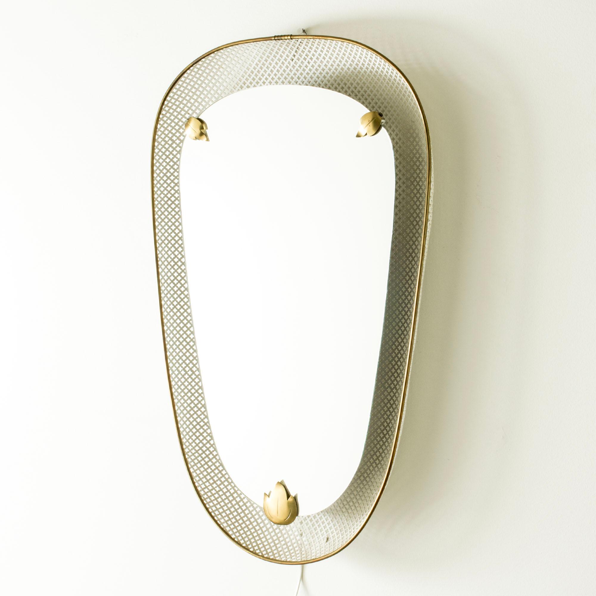 Elegant miroir mural moderne suédois, éclairé par l'arrière de façon à ce que la lumière brille autour du bord du verre du miroir. Fabriqué en métal laqué blanc avec un motif de trèfle découpé, un bord en laiton et des feuilles décoratives.