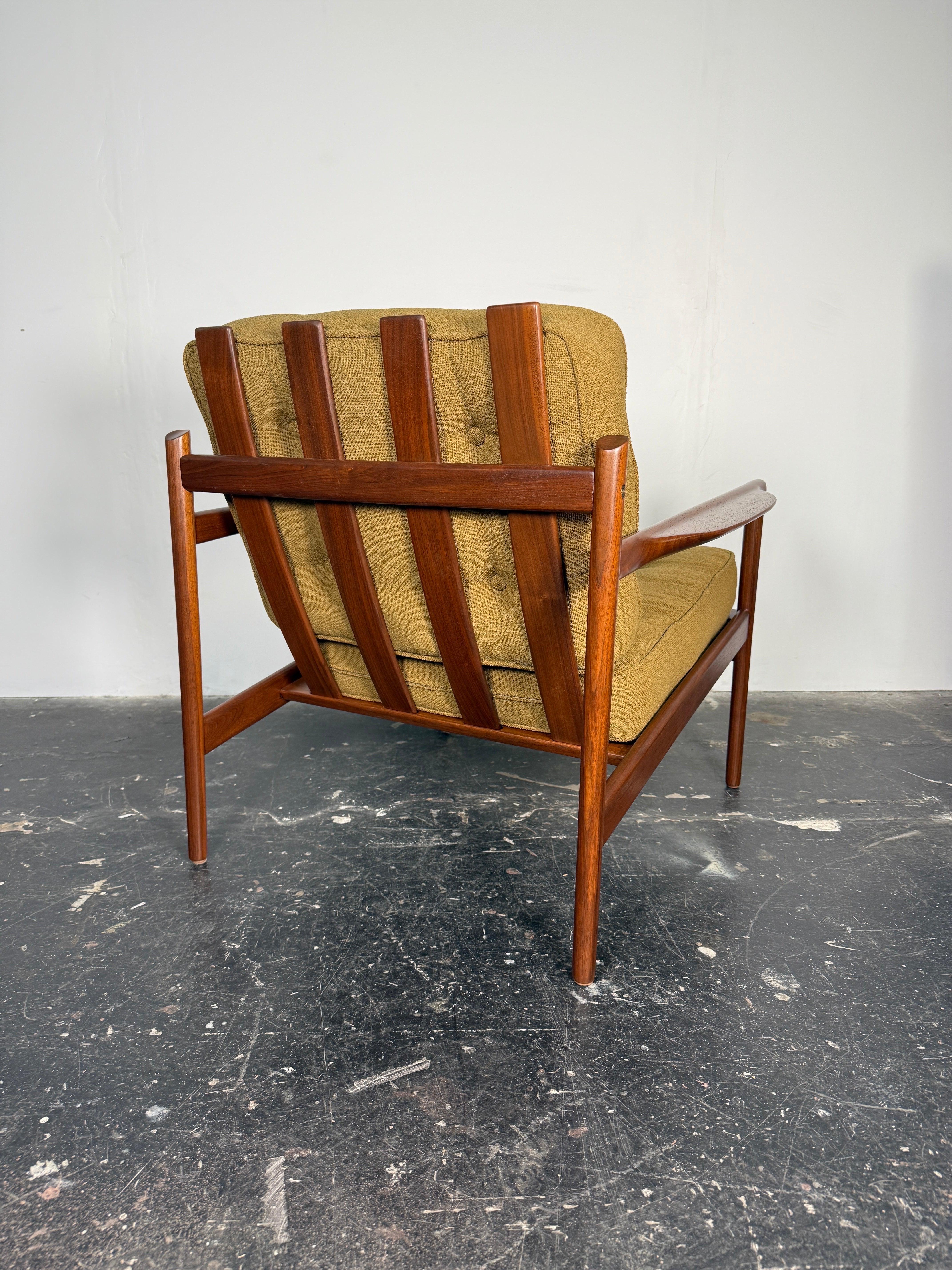 Superbe chaise longue conçue par Ib Kofod-Larsen et fabriquée au Danemark vers les années 1960. Ce design moderne danois se caractérise par un cadre en bois de noyer massif, quatre grandes lattes faisant office de dossier et des accoudoirs