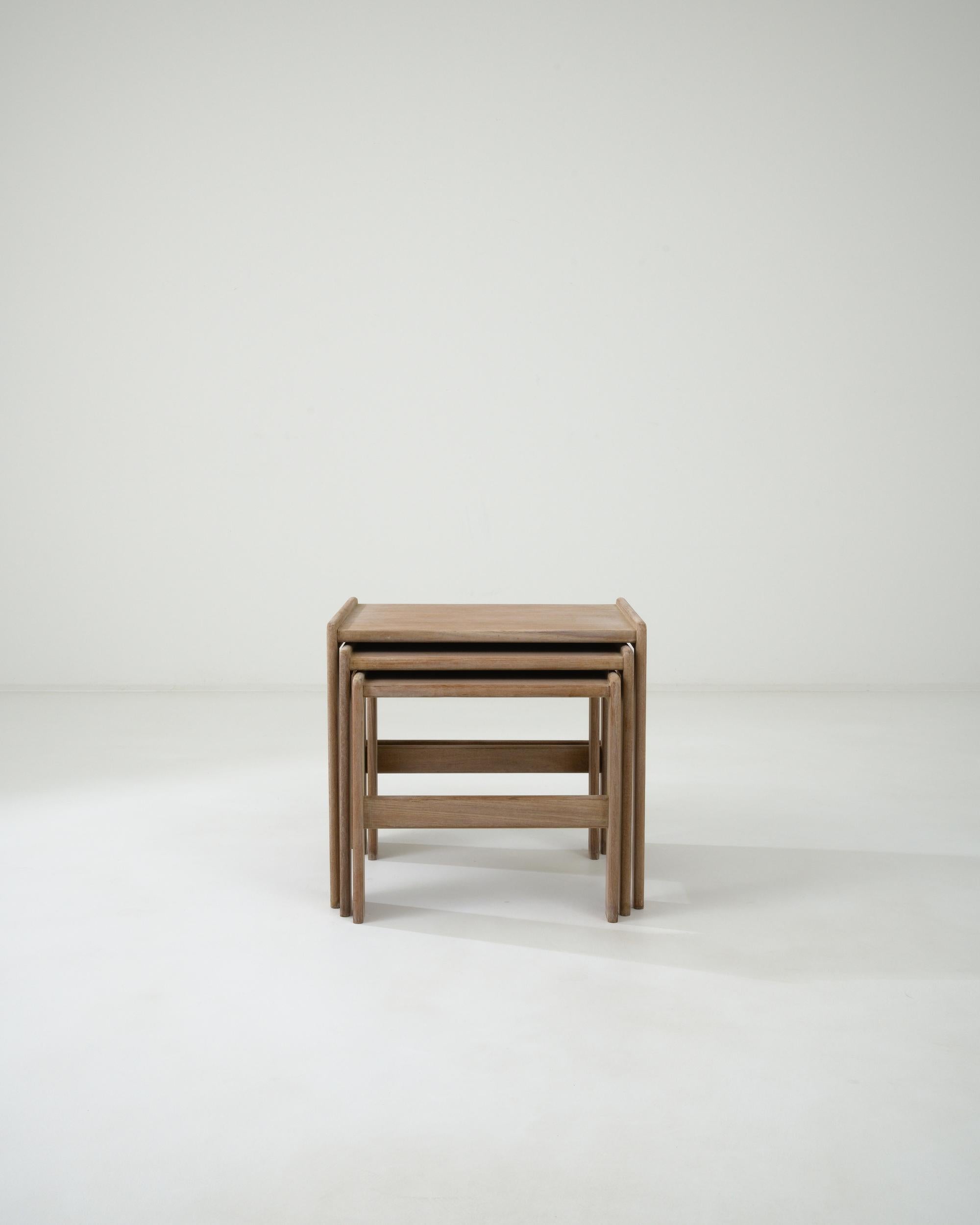 Built in Scandinavia during the 20th century, this set of nesting tables flaunts impeccable symmetry expressed through the gentle interplay of sleek outlines of their geometric bases and smooth tabletops. The use of bleached teak, often associated