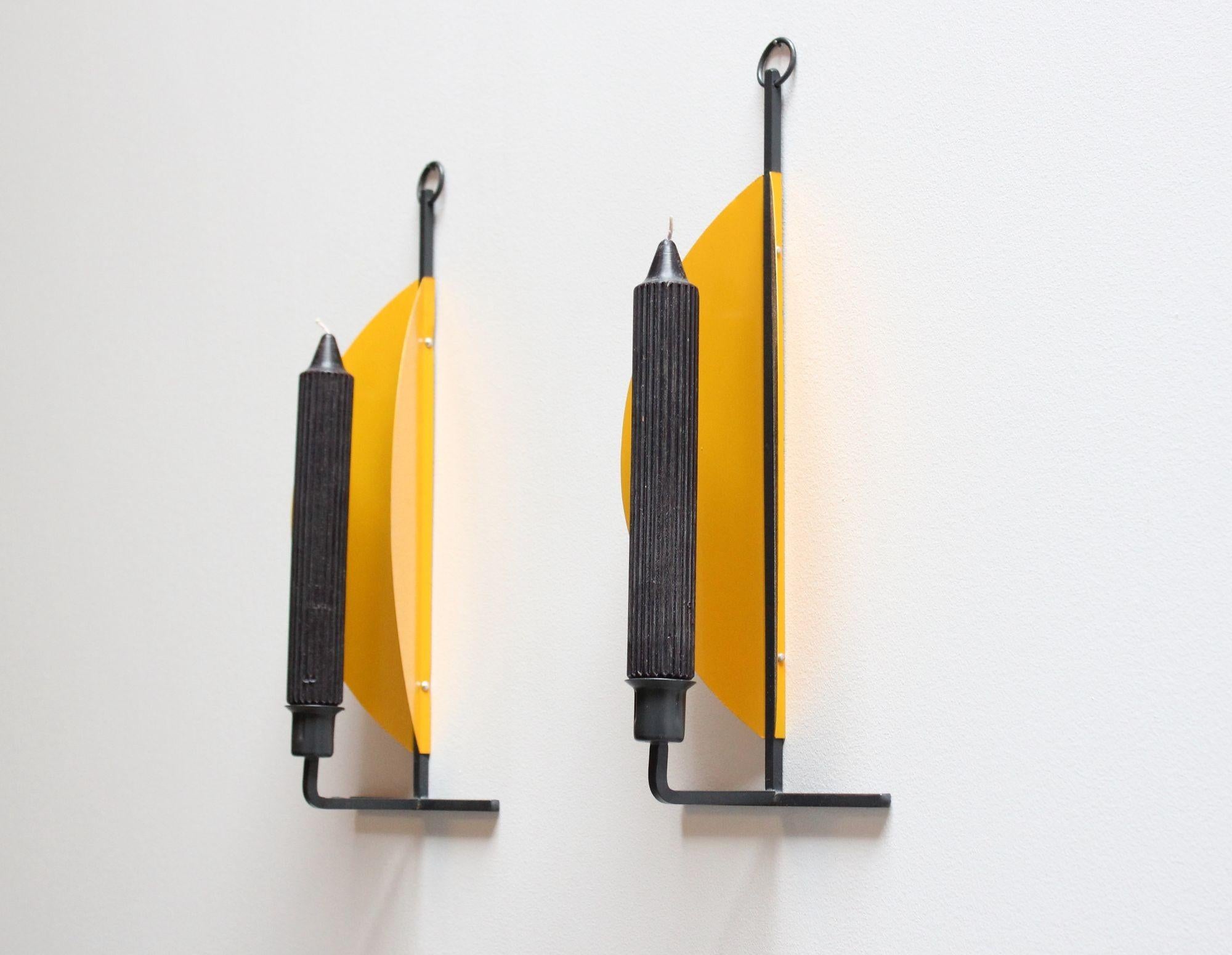 Stylish, modernist candle scones (ca. 1960s/1970s, Denmark). Composed of vibrant yellow semi-circular discs mounted to a charcoal metal stem at an angle to give the appearance of cradling the candle and better containing the light they emit.
Each