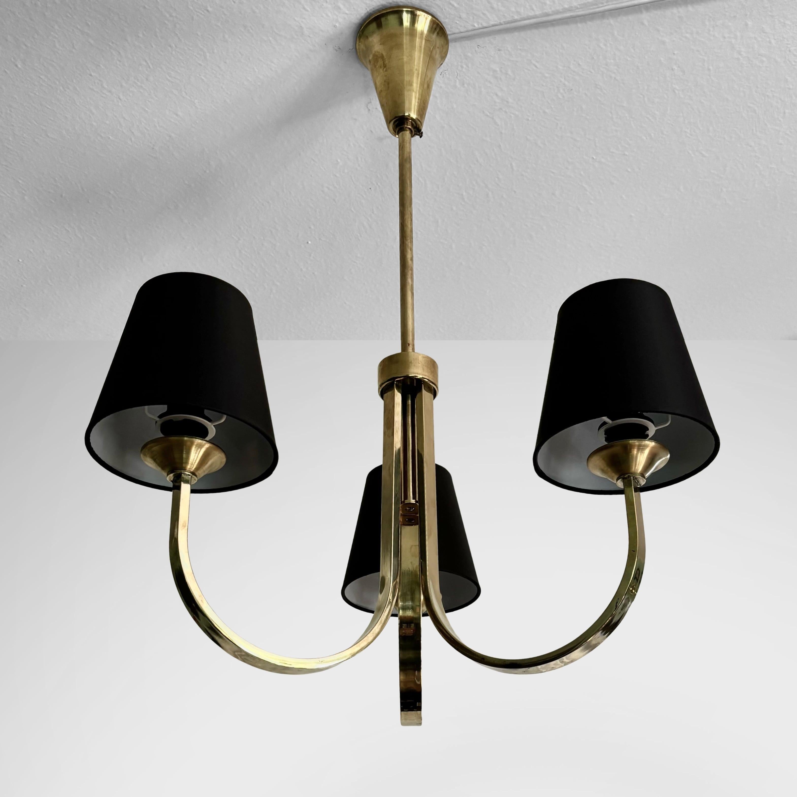 Un grazioso lampadario modernista scandinavo realizzato in ottone lucido, con tre bracci curvi che ospitano paralumi neri. Ha una calotta conica montata vicino al soffitto. Probabilmente prodotto da un produttore non identificato in Danimarca negli