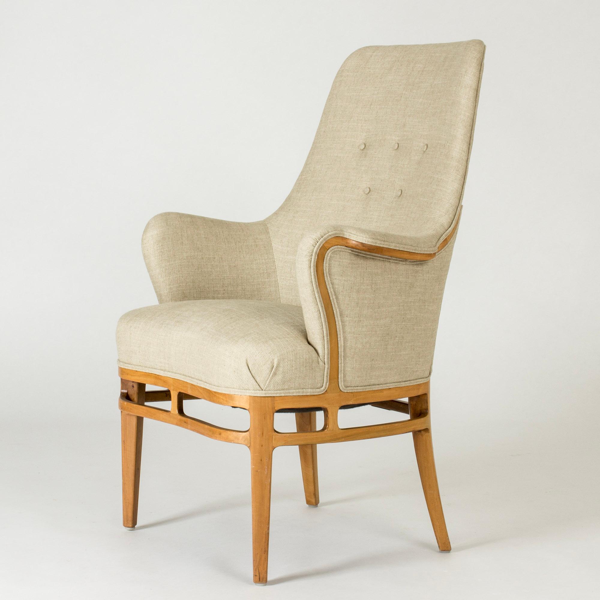 Elegant lounge or armchair by Carl-Axel Acking, made in walnut and upholstered with linen. Beautiful carved decor around the base of the seat and lines of wood following the curves of the armrests and back. Decorative piping.