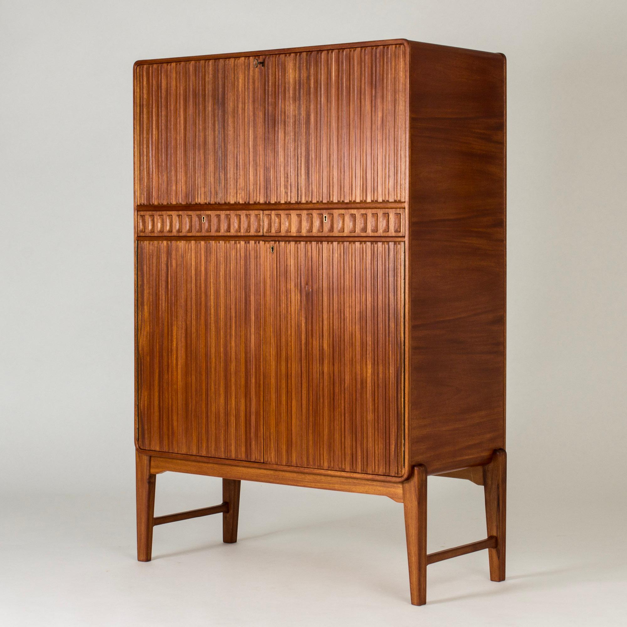 Striking unique mahogany cabinet by Swedish architect Carl Cederholm, in a luxurious design. Elegant relief pattern of stripes on the fronts and drawers, subtle sculpted details. Dry bar top part with a glass shelf.