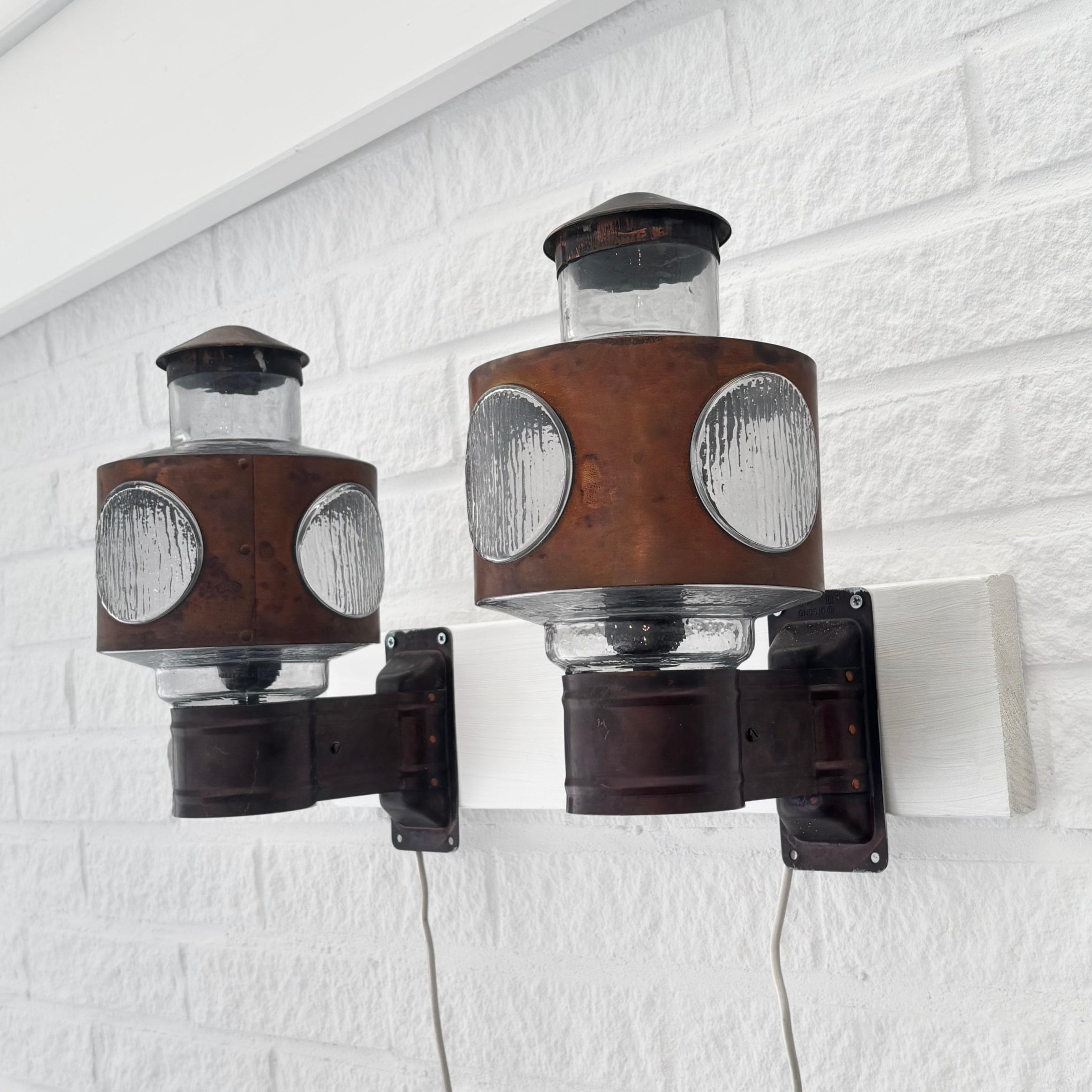 A pair of Scandinavian modernist outdoor facade lamps, model 340, crafted from copper and glass. Featuring a sturdy wall mount supporting a sculptural glass shade, partially covered in copper. Produced by the Swedish lighting manufacturer Gnosjö