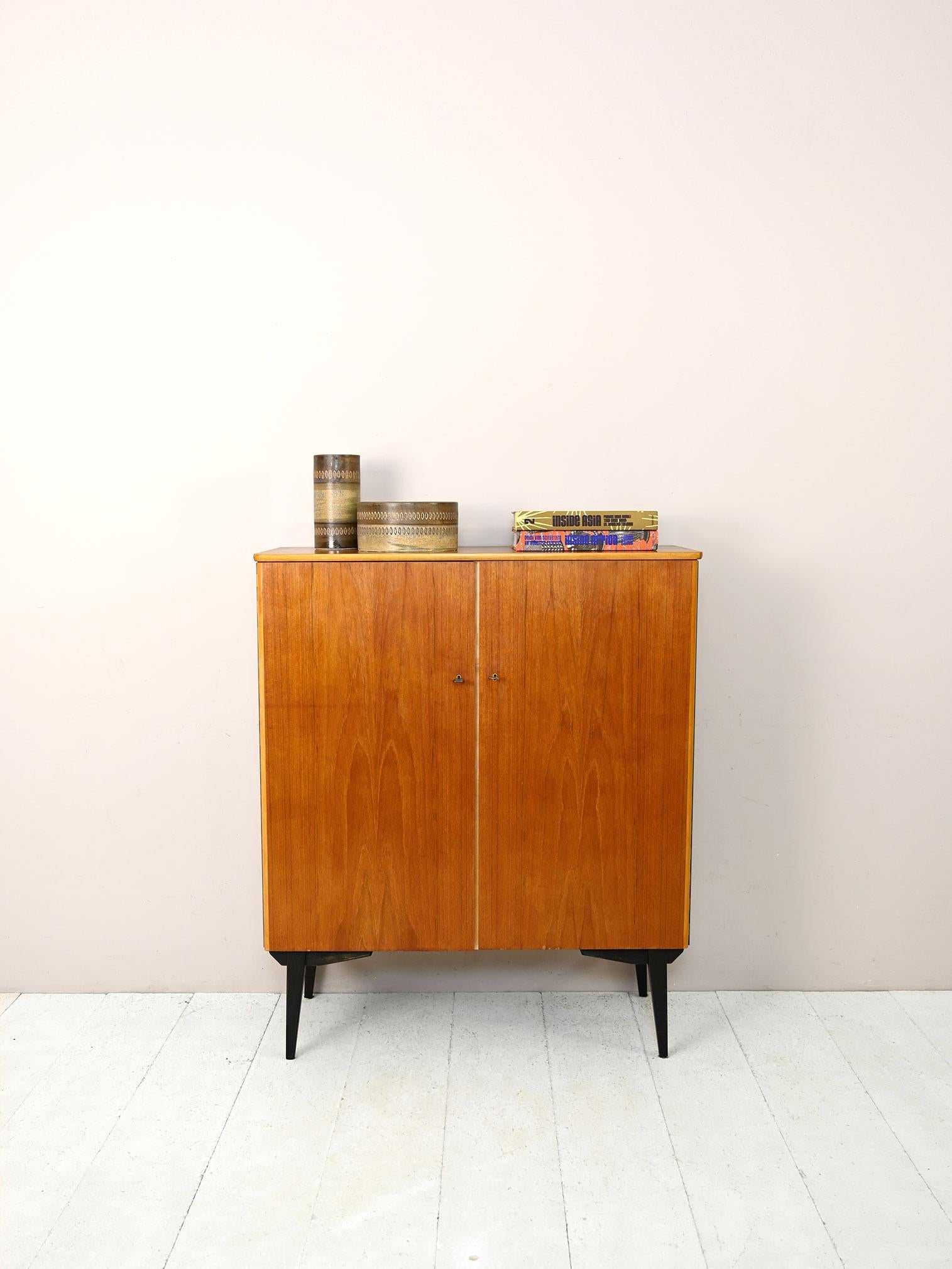 Vintage 1960s teak sideboard with black painted details.

This modern cabinet consists of a compartment equipped with shelves closed by two hinged doors equipped with a lock.
Characterized by simple and essential lines but enriched by some