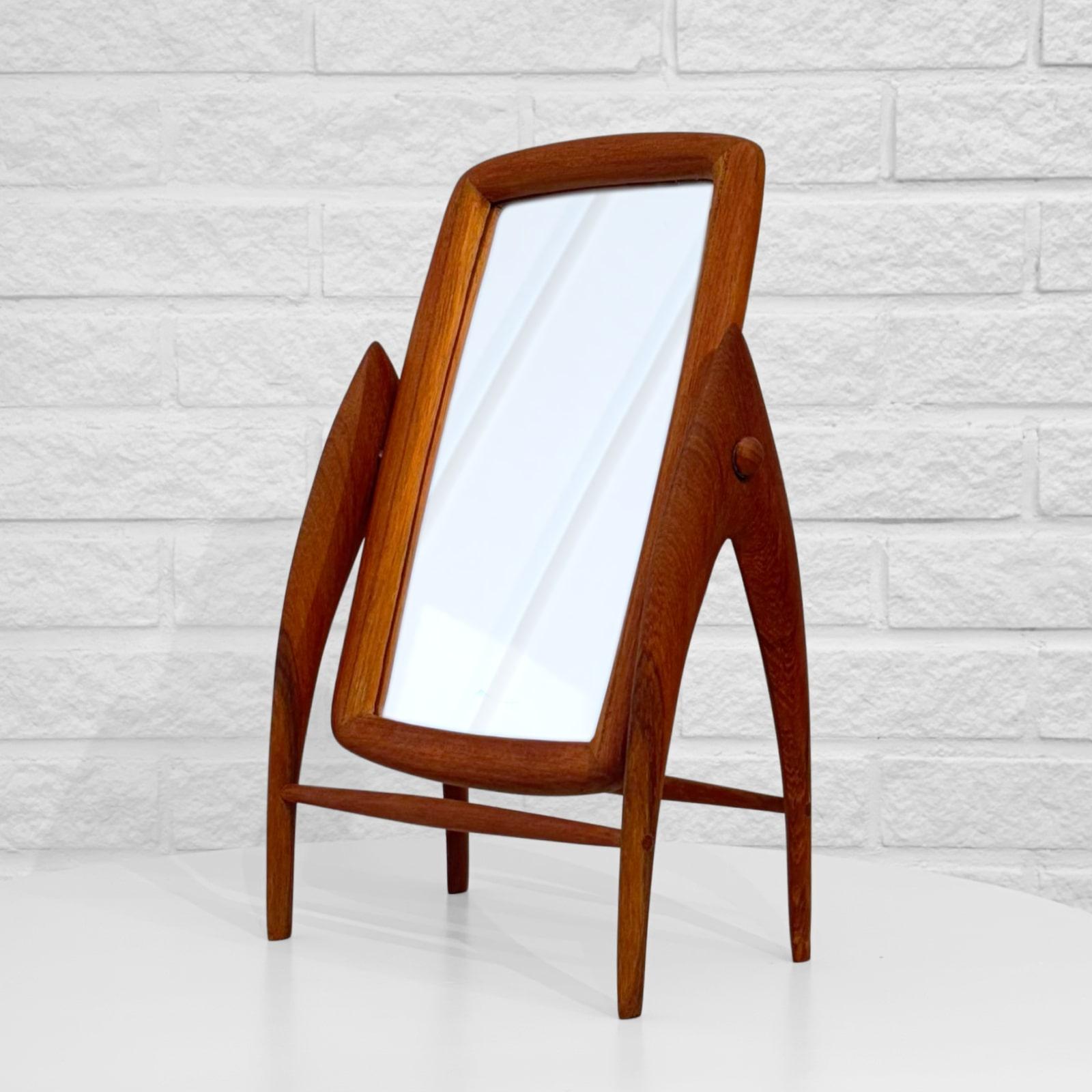 A modernist Scandinavian vanity mirror, crafted from solid teak by an unidentified Swedish manufacturer in the 1950s. Sculptural bow-shaped legs hold a rectangular, tiltable mirror for maximum flexibility. The sculptural form and soft, streamlined
