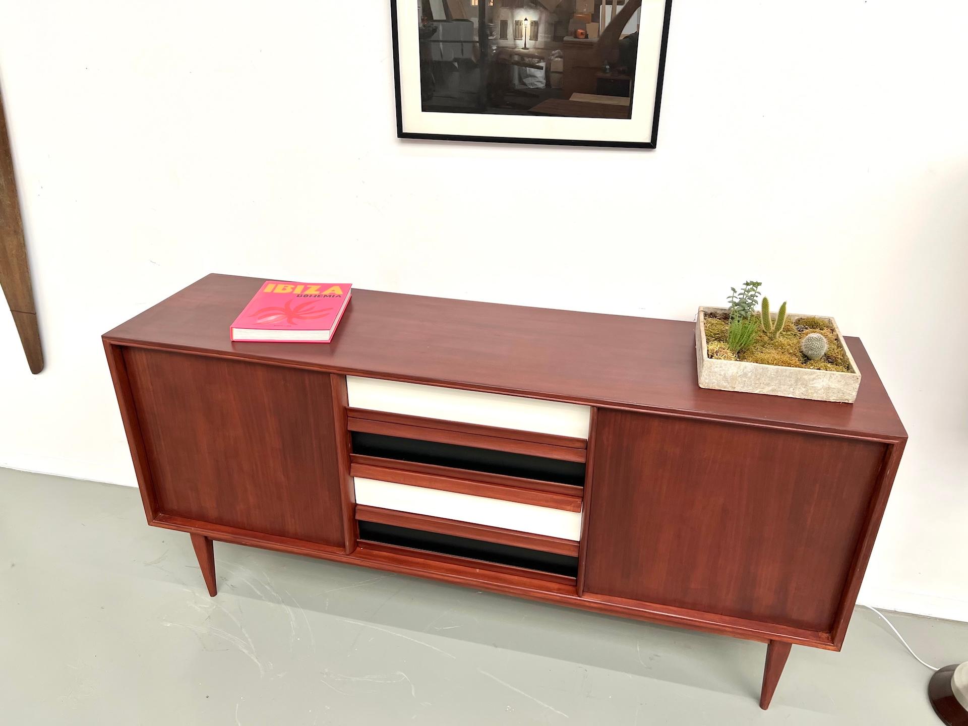 Maison Lecan presents this Scandinavian modernist teak sideboard from the 1970s.

Featuring elegant tapered compass legs and clean Nordic lines, it offers a central section with four contrasting drawers, flanked by two doors concealing spacious