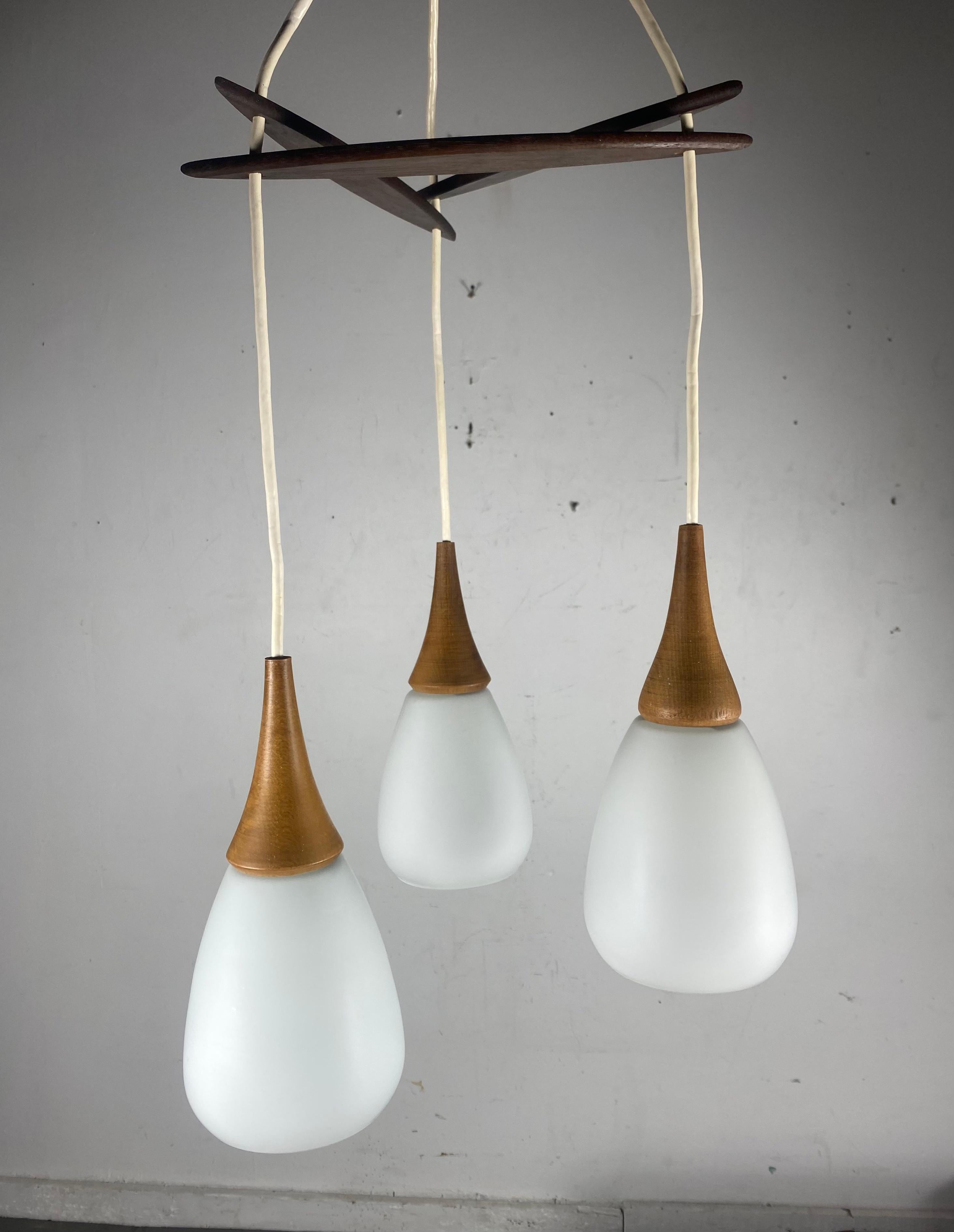 Triple tear drop pendant light. Danish design, circa 1955.
Opaline glass globes from Holmegaard with teak tops hung from an adjustable r three pronged rosewood canopy.