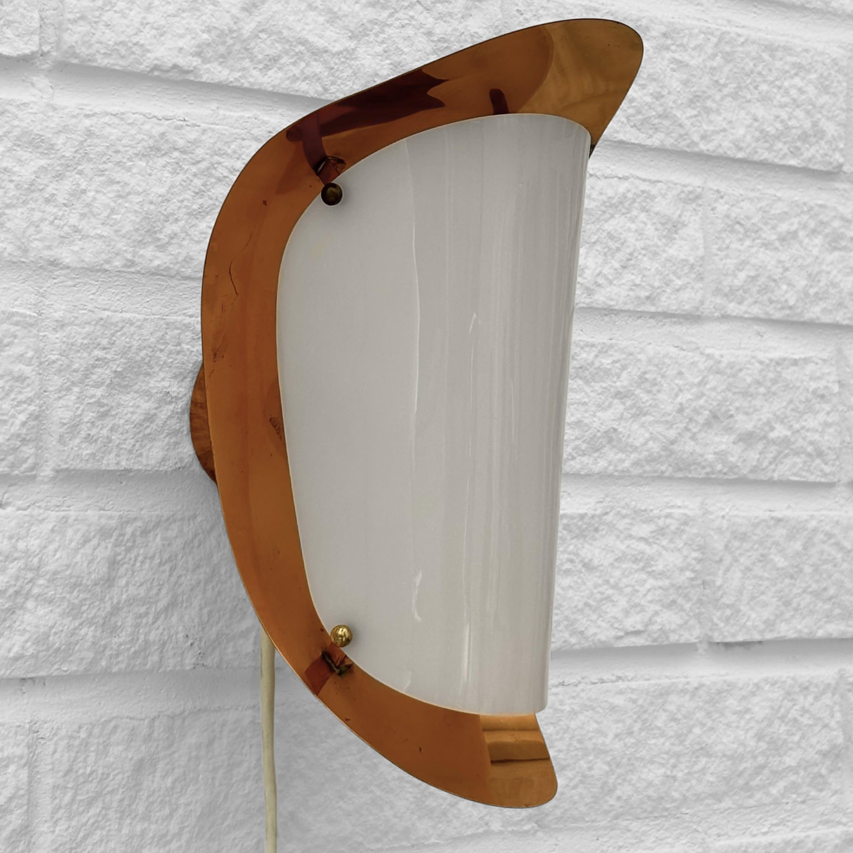 A Scandinavian modernist wall lamp produced by Swedish manufacturer Karlskrona Lampfabrik in the 1960s. Crafted from copper, it features an organically shaped reflector and a white acrylic diffuser held in place by four small brass spheres. With the