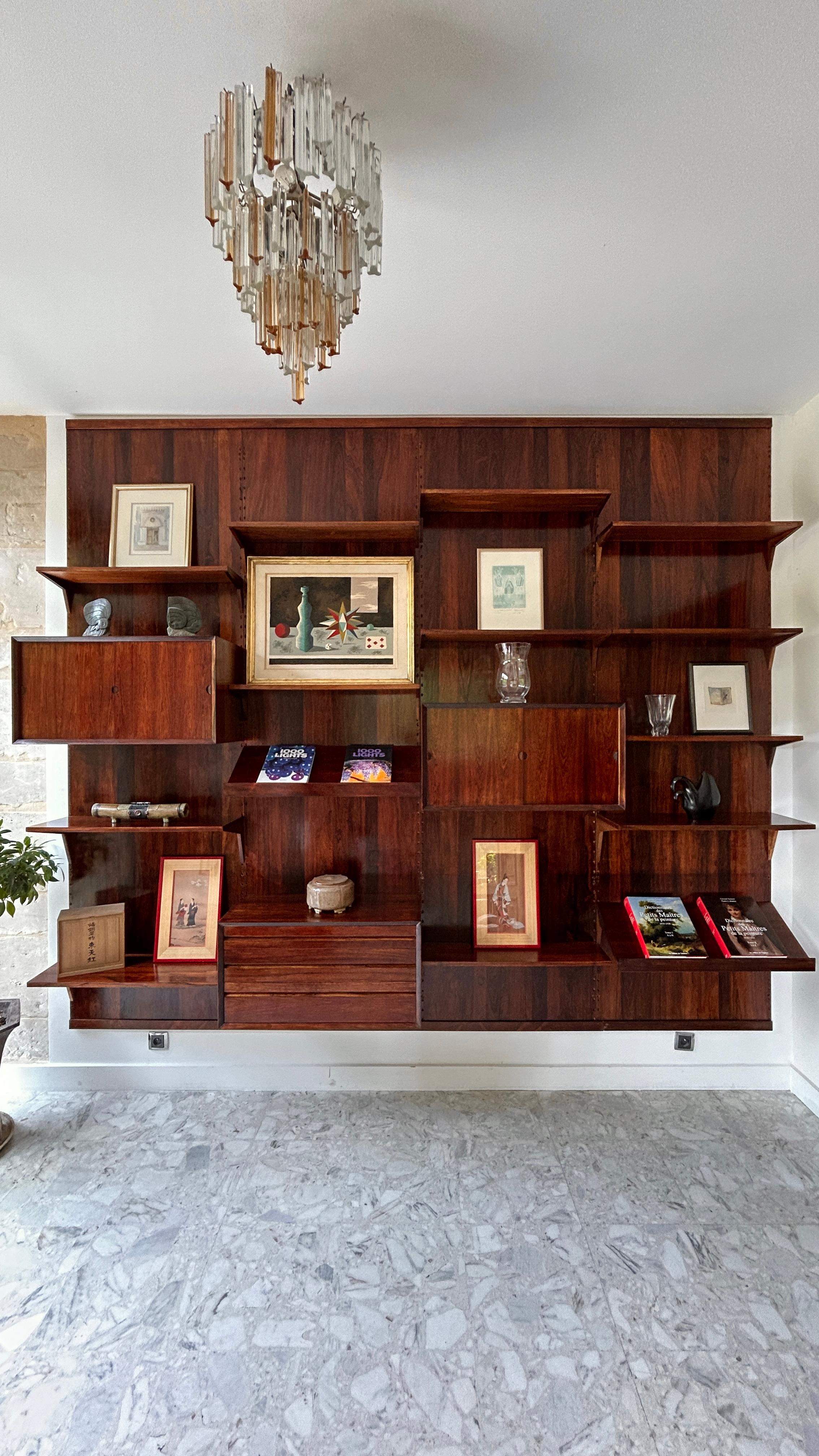 Bellissima libreria modulare a parete del famoso architetto danese Poul Cadovius, impiallacciata in palissandro. Questa libreria, montata su 4 pannelli a parete, comprende numerosi scaffali, due scaffali ad ante scorrevoli, una cassettiera e due