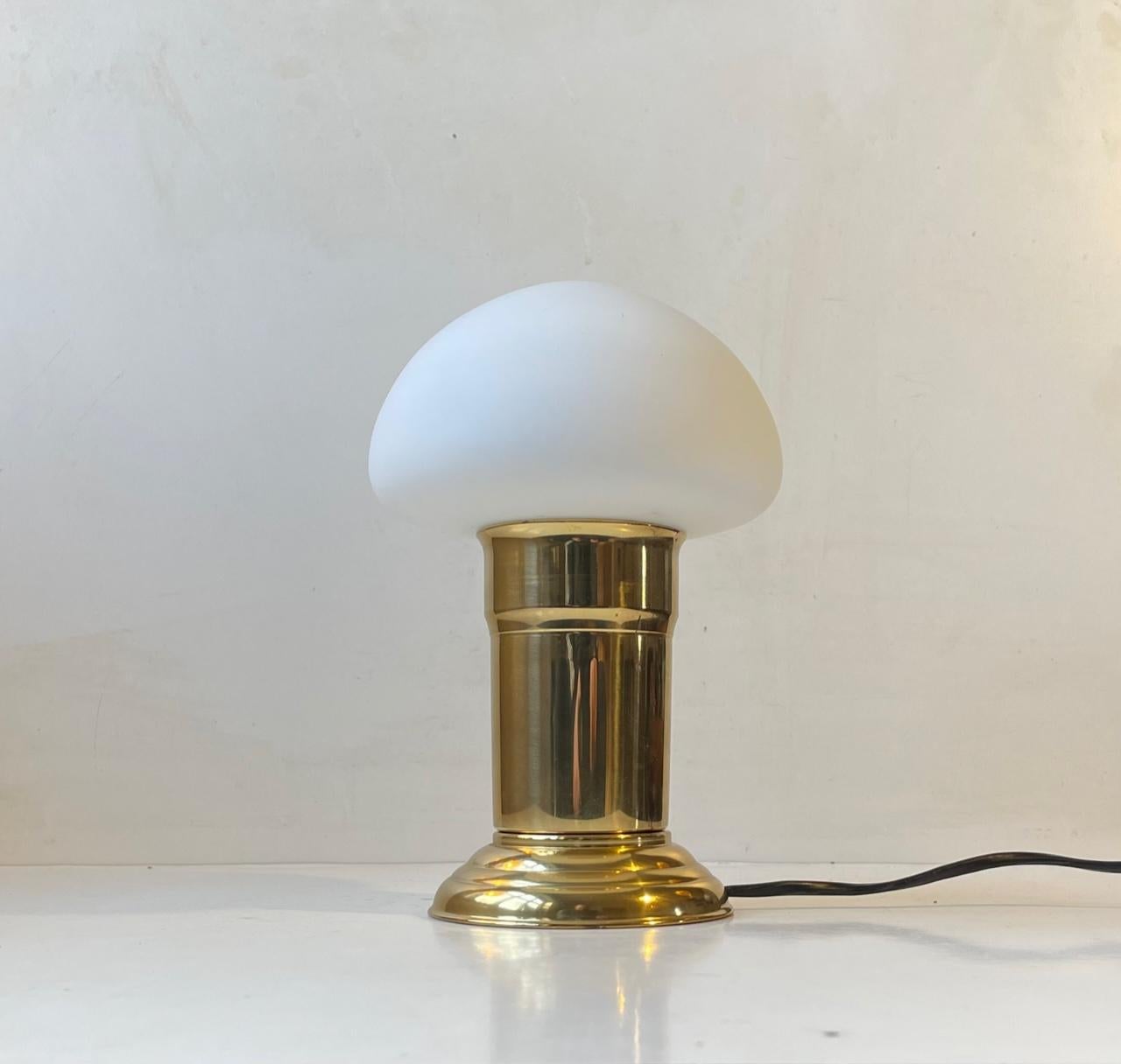 Unusual and petite table light executed in brass and featuring a mushroom shaped shade in matte/frosted glass. It has an on/of switch to its cord. Unknown Scandinavian maker/design circa 1970-80. Measurements: H: 24 cm, D: 14 cm.

For the US. It