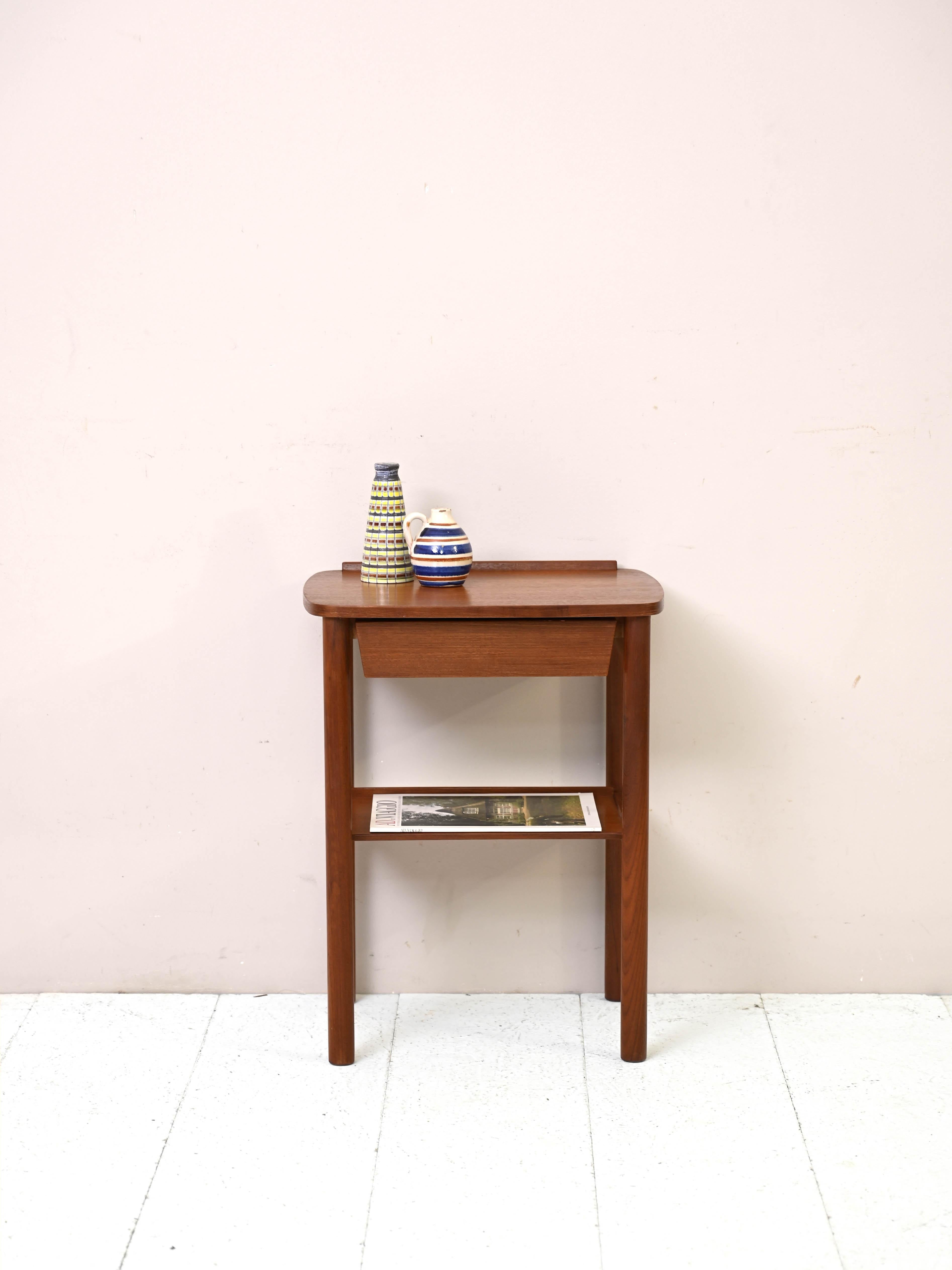 Vintage side table with drawer and magazine rack top.

A small bedside table in excellent original preservation.
It is distinguished by its compact shape and domed-edged top. A drawer and magazine rack top is present. The conical shaped legs make