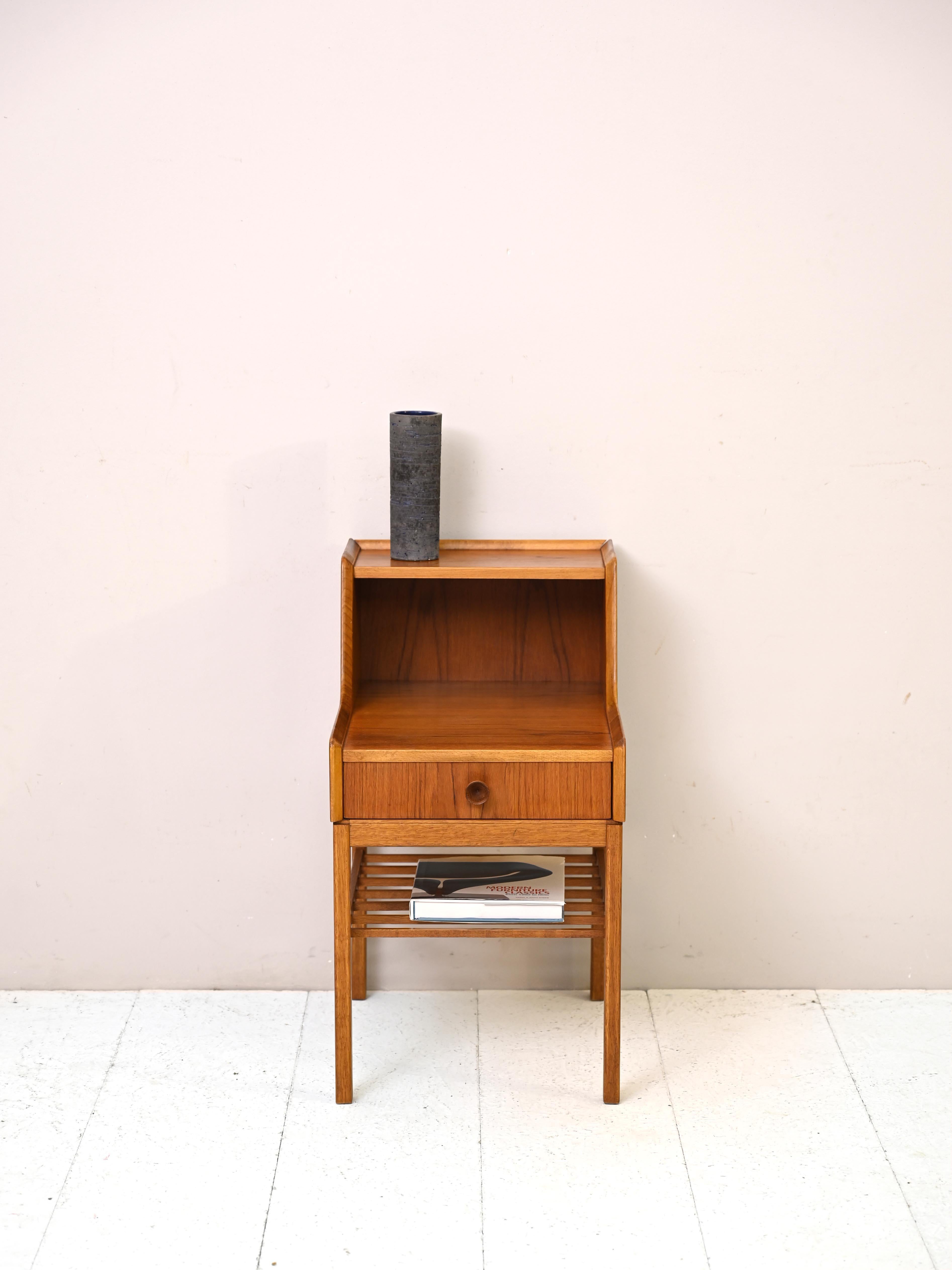 Swedish teak nightstand from the 1960s.

This original bedside table is distinguished by its unusual shape given by the double shelf, which is very useful for resting the lamp and keeping the second shelf free. 
There is also a convenient drawer