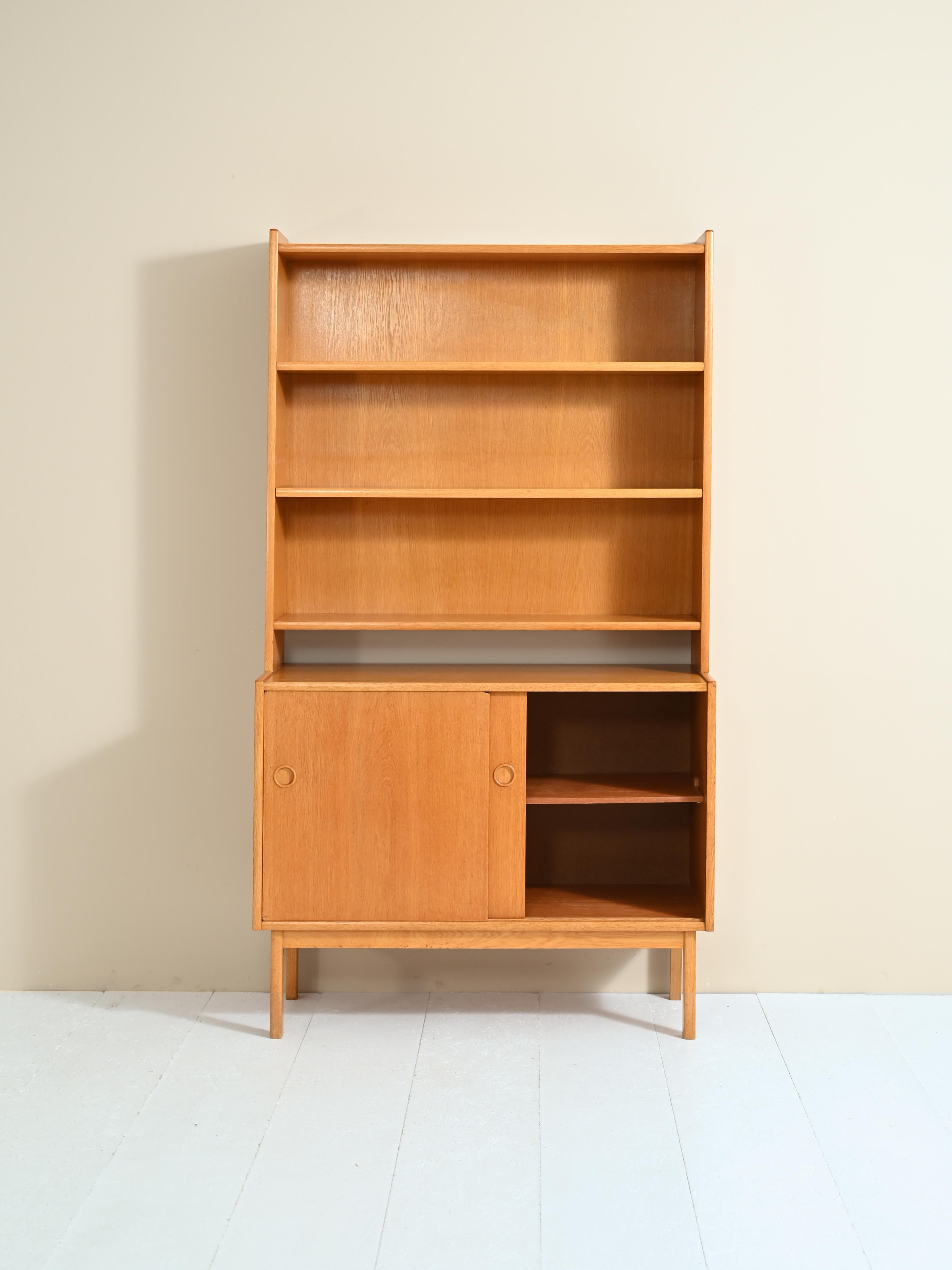 Bookcase with shelving and cabinet, 1950s/60s.
Original vintage cabinet from Scandinavia consisting of two parts. The upper part is a bookcase equipped with adjustable height shelving, the lower part is a cabinet equipped with two sliding