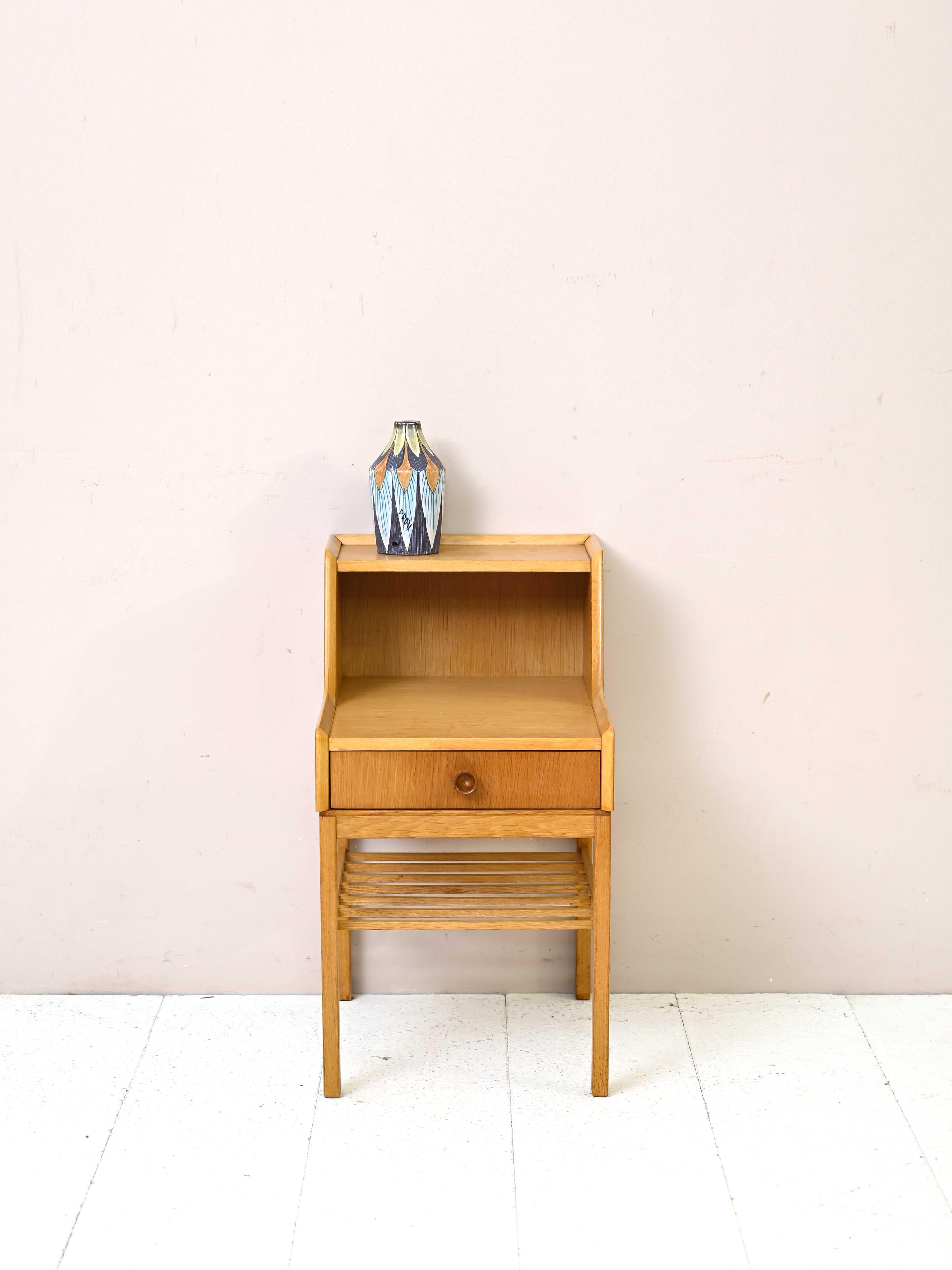 1960s vintage nightstand.

This original nightstand is distinguished by its unusual shape given by the double shelf, which is very useful for resting the lamp and keeping the second shelf free. 
There is also a convenient drawer and a magazine