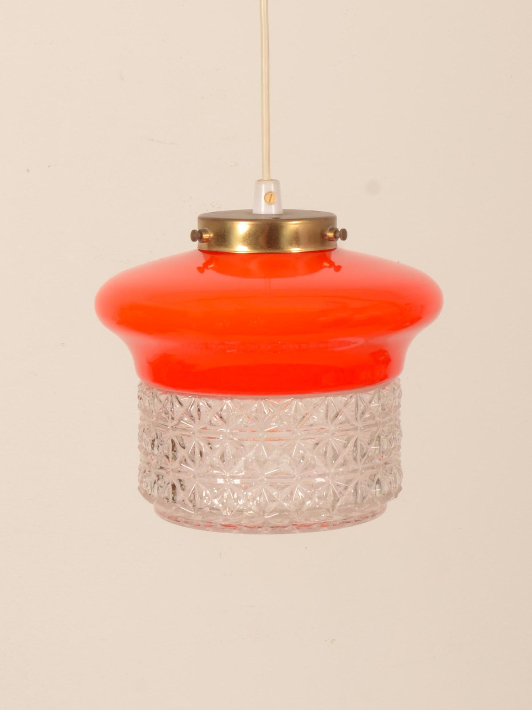 Lámpara colgante de cristal con pantalla de cristal naranja en la parte superior y cristal estructurado transparente en la parte inferior. Equipada con una toma E27. Fabricado en la década de 1970 en Suecia por ÖIA Belysning. Otro con la parte