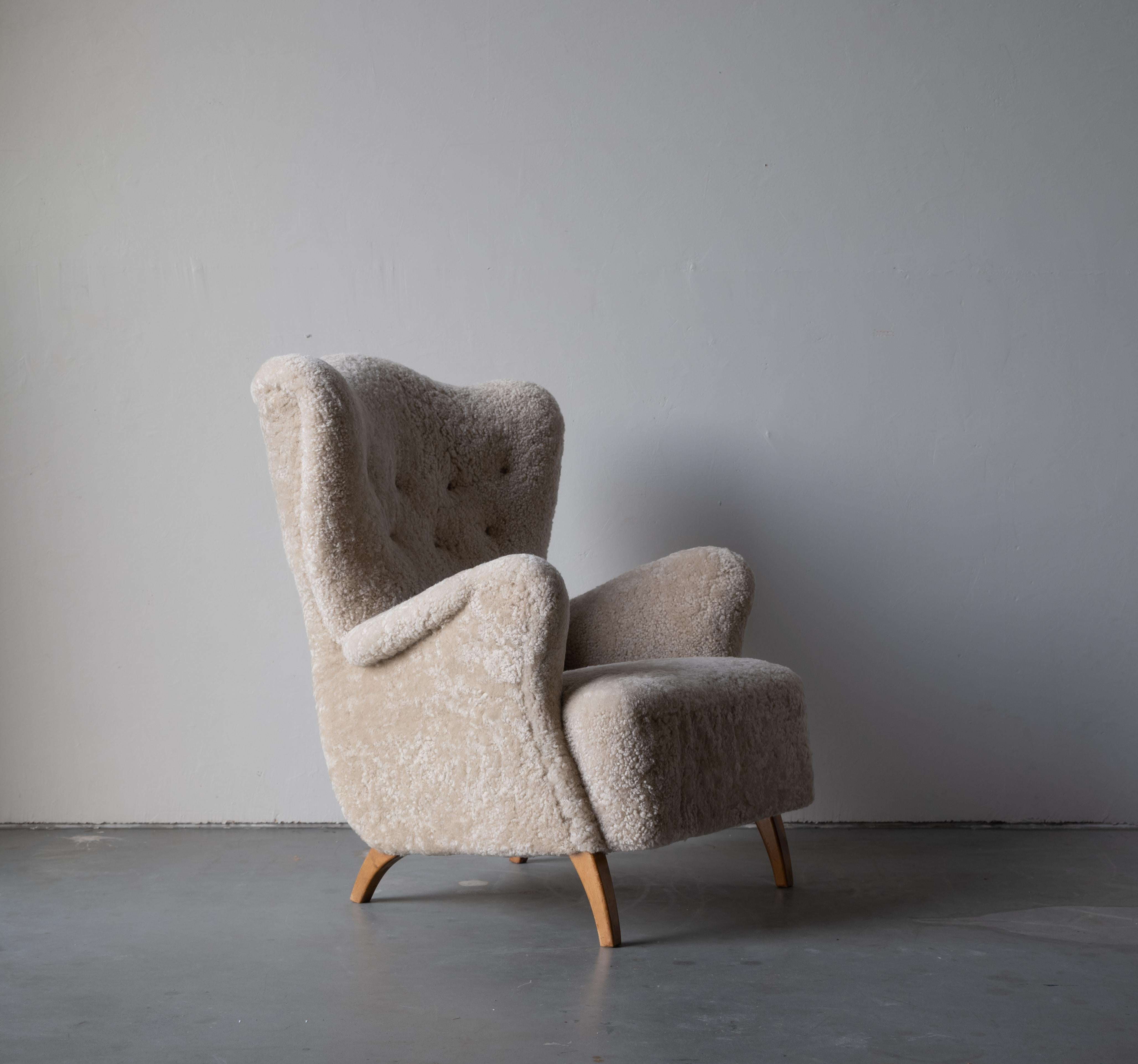 An early modernist lounge chair/armchair. Oak legs, reupholstered in beige lambskin / sheepskin. Produced in the 1940s in Scandinavia. 

Produced in the same era as works by Philip Arctander, Viggo Boesen, Flemming and Mogens Lassen, Kurt Ostervig