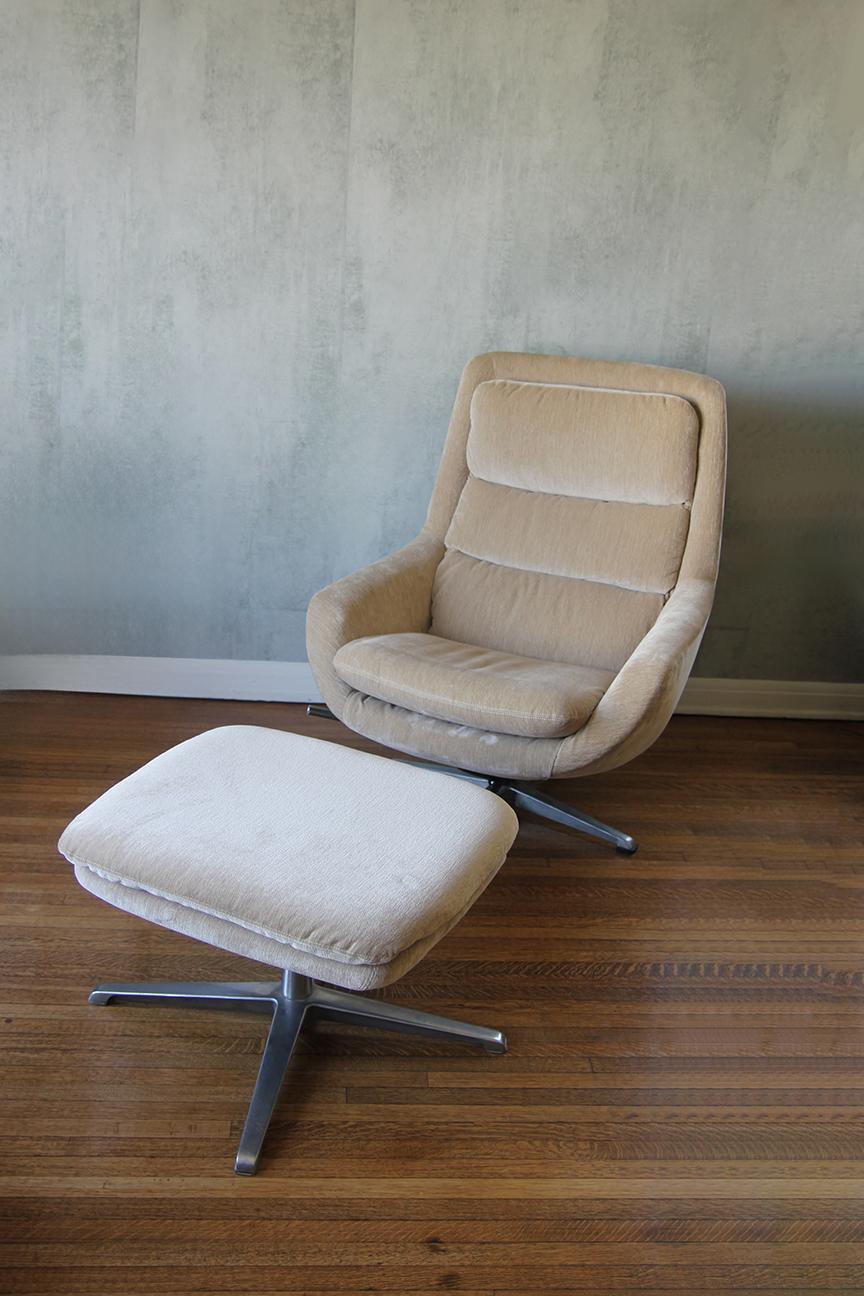 Este sillón reclinable y puf de estilo escandinavo tiene una sólida estructura de metal y tapicería color crema. El sillón reclinable es de un cómodo color crema/arena y descansa sobre una base redonda de metal que gira 360 grados. La otomana está