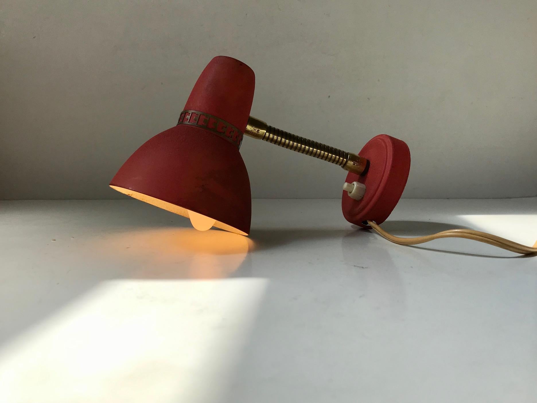Small adjustable wall lamp made from brass and aluminium. The pastel red lacquer has been applied in such a way that its surface mimics leather. It was made in Scandinavia during the 1950s, probably by ASEA or Falkenberg.