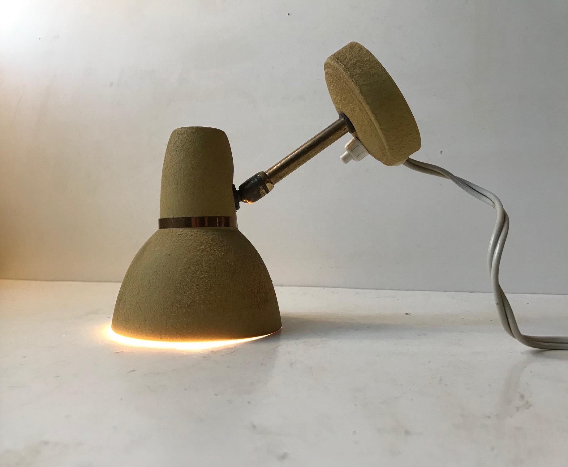 Small adjustable wall lamp made from brass and aluminium. The pastel mustard yellow lacquer has been applied in such a way that its surface mimics leather. It was made in Scandinavia during the 1950s, probably by ASEA or Falkenberg.