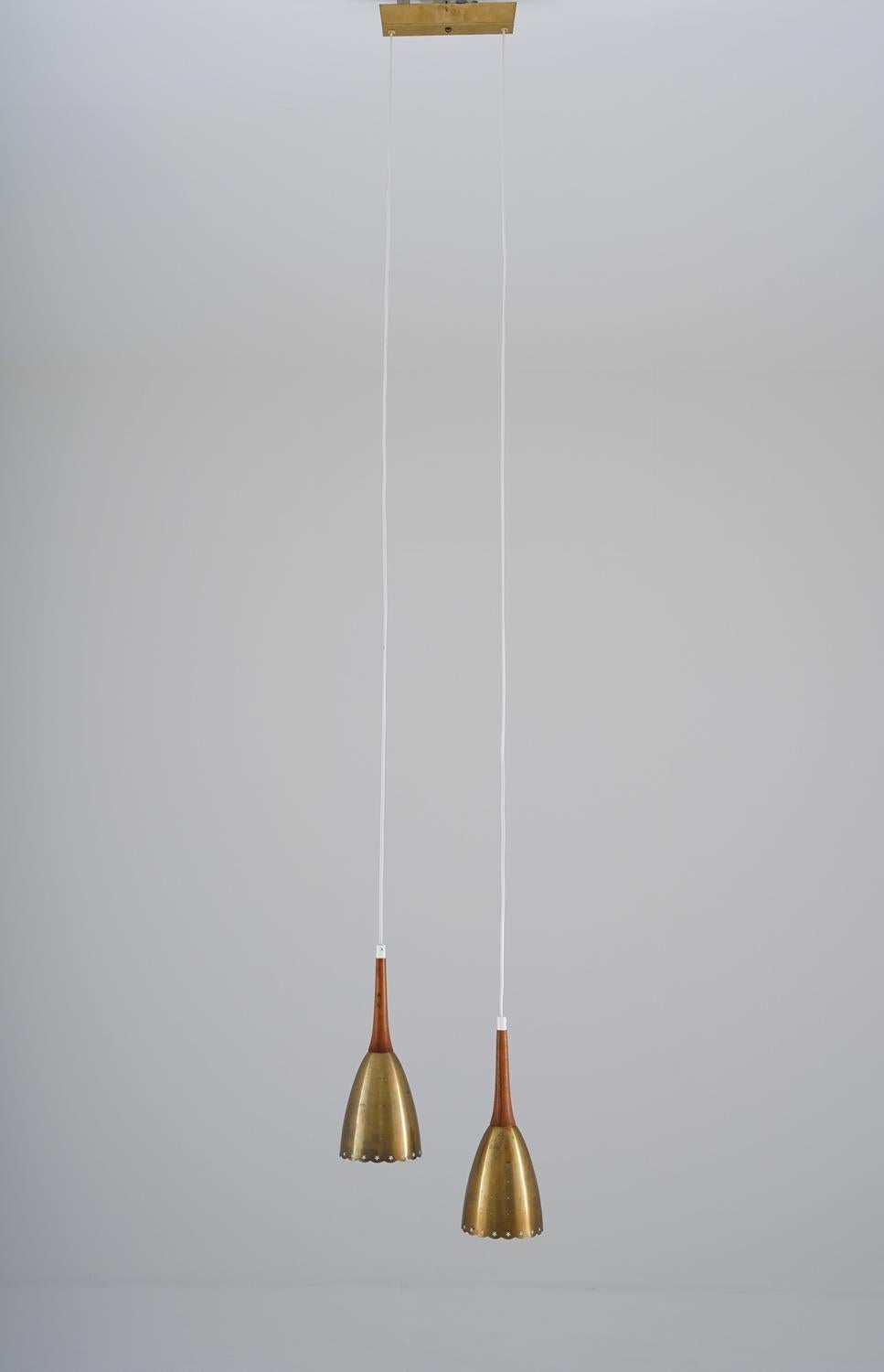 Elegant pendant in brass with wooden details, manufactured in Denmark, 1950s. 
The lamp consists of two pendants, hanging from a brass canopy. The shades are made of brushed perforated brass and look beautiful when lit. 

Condition: Good original