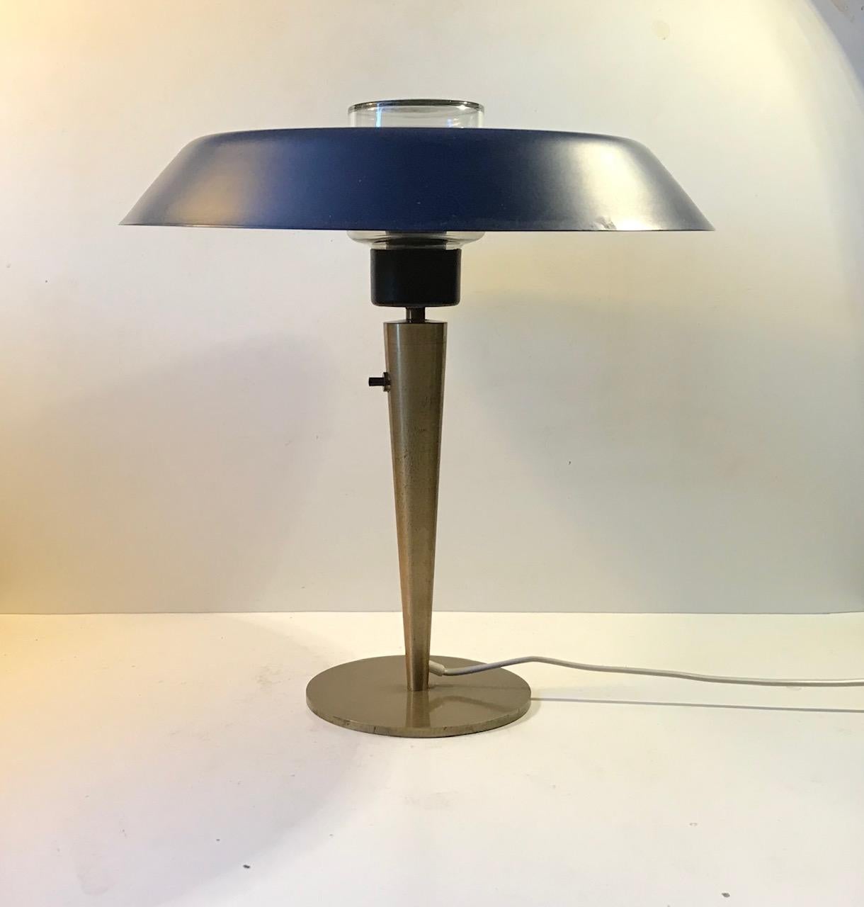 Unidentified Danish maker in the style of Holm-Sorensen, Louis Kalff. This desk or table lamp has a solid brass and features a discretely placed on/off switch and a large petrol-blue metal shade set upon a clear glass inner-shade.