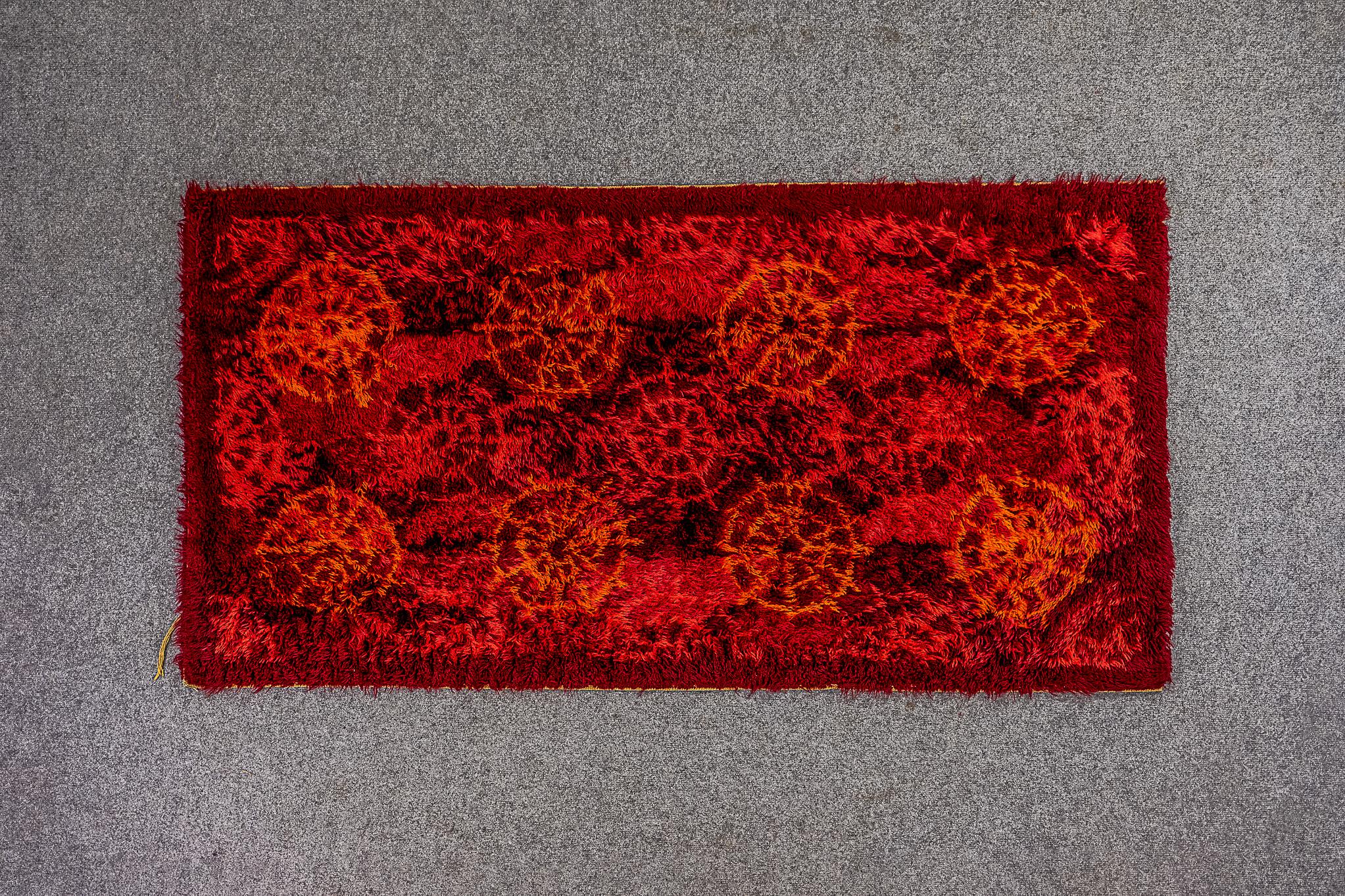 Tapis scandinave en laine, datant des années 1960. Ce tapis brillant et saisissant peut être utilisé comme revêtement mural ou comme tapis de sol. Le tapis représente un motif de roue abstrait et rythmique dans un jeu de couleurs rouge et marron.