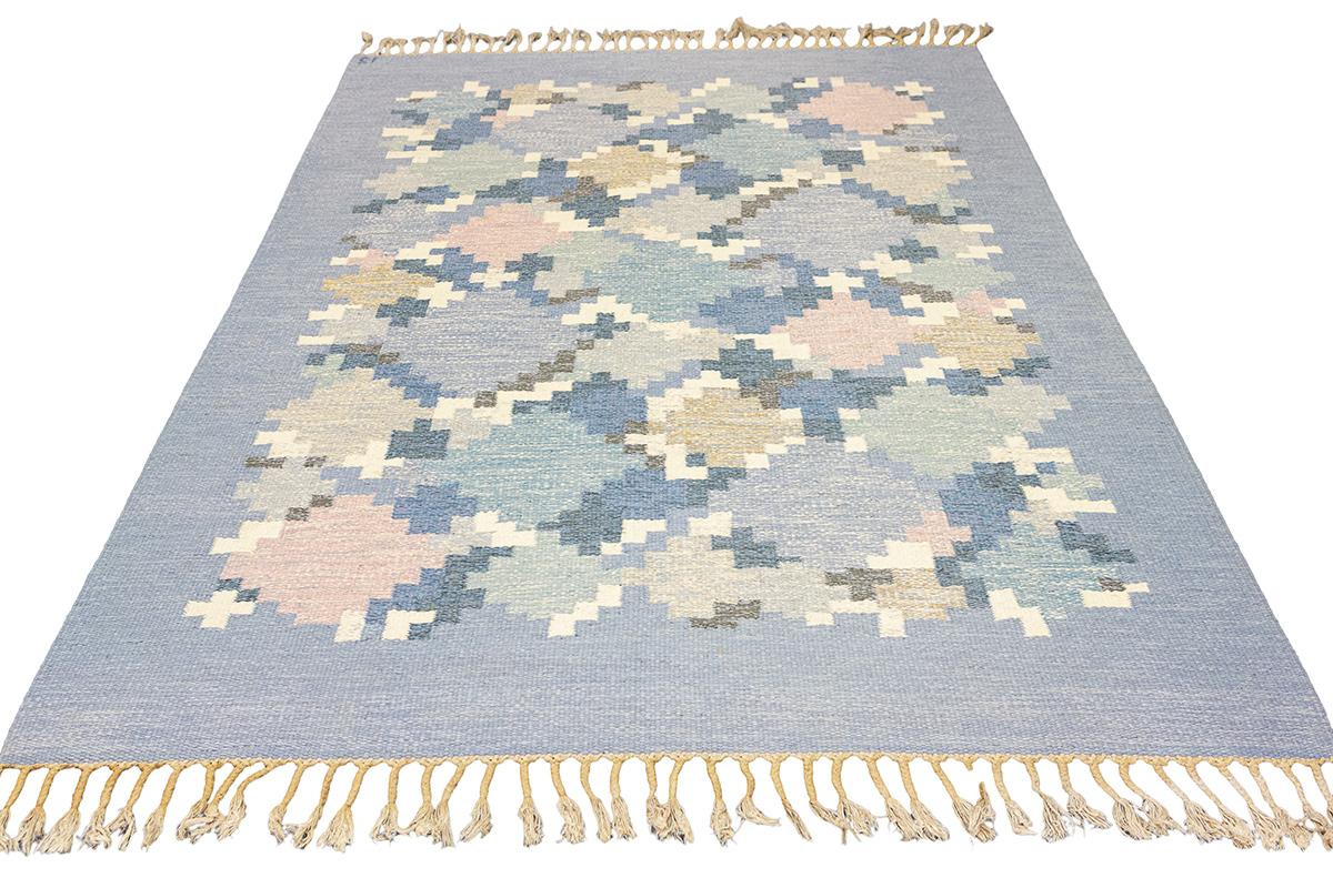 Questo tappeto scandinavo Rollakan  affascina con il suo bellissimo gioco di colori e motivi geometrici, fondendo l'artigianato tradizionale con l'estetica moderna. Caratterizzato da un'armoniosa composizione di motivi floreali e geometrici in una