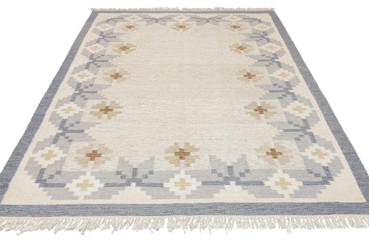 Step into the world of design with this classic Scandinavian rug rollakan, a piece that exudes both warmth and style. Its subtle yet captivating pattern features a balanced array of geometric shapes and crosses, delicately woven in soft, natural
