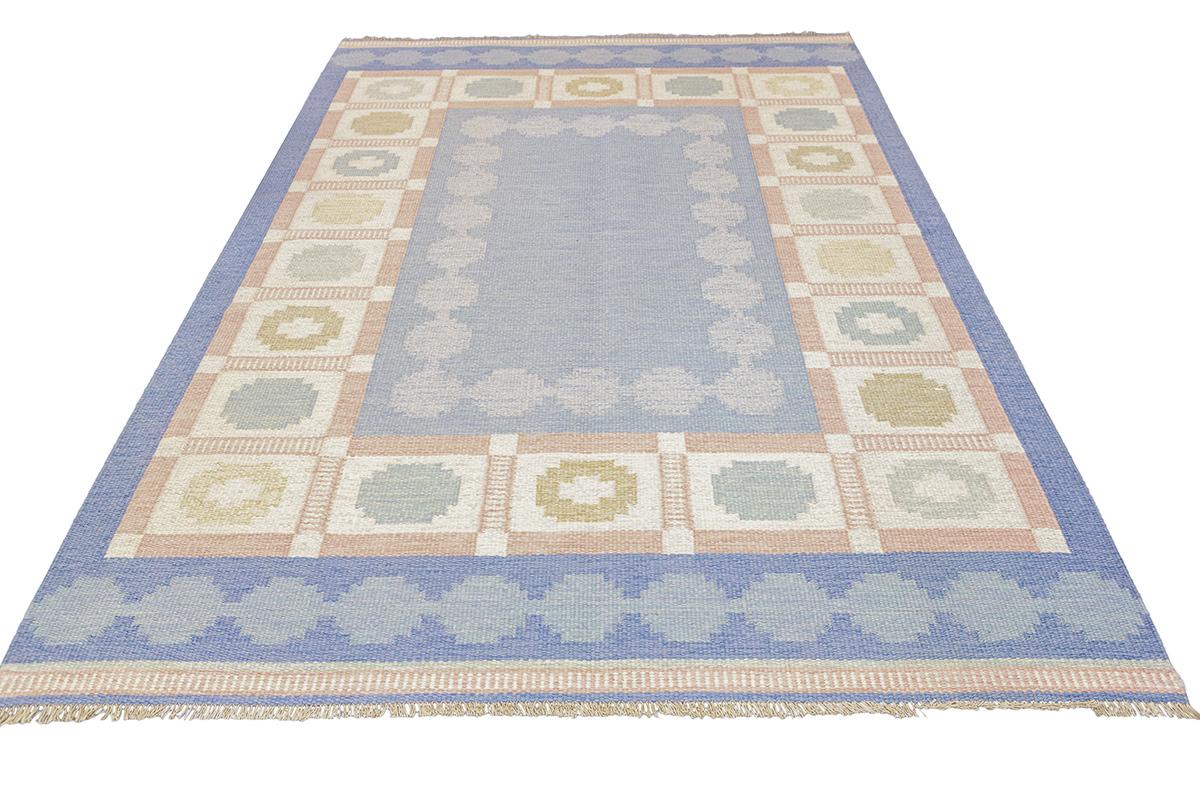 Dieser raffinierte skandinavische Teppich Rollakan zelebriert die kühle Eleganz, die zeitlose Anziehungskraft und das tadellose Designgefühl der nordischen Handwerkskunst. Der Teppich besteht aus einer ruhigen Palette von sanften Blau- und
