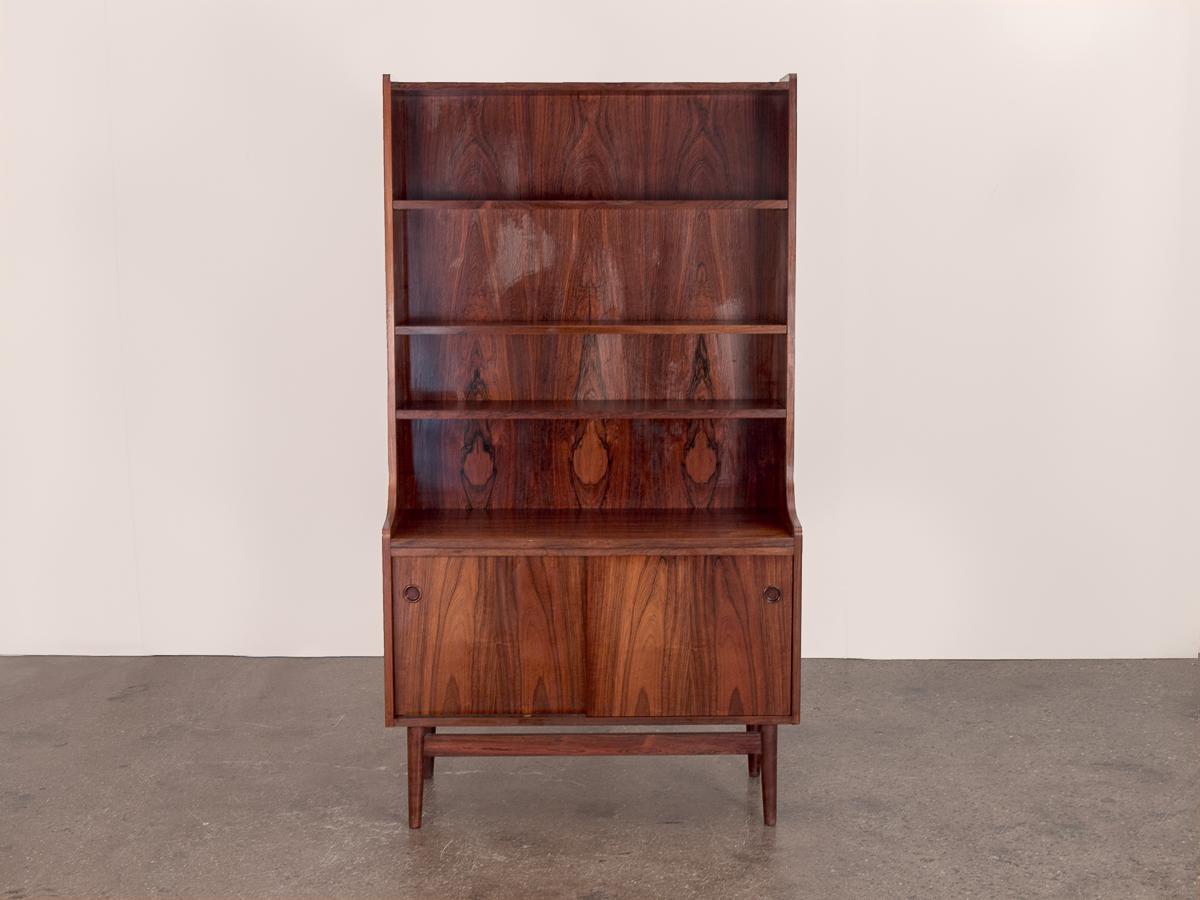 Clean lines and timeless design underscore this elegant rosewood bookcase. Sturdy and substantial, the bookcase features three adjustable shelves for open display and two covered storage areas at its base. In excellent vintage condition; the rich