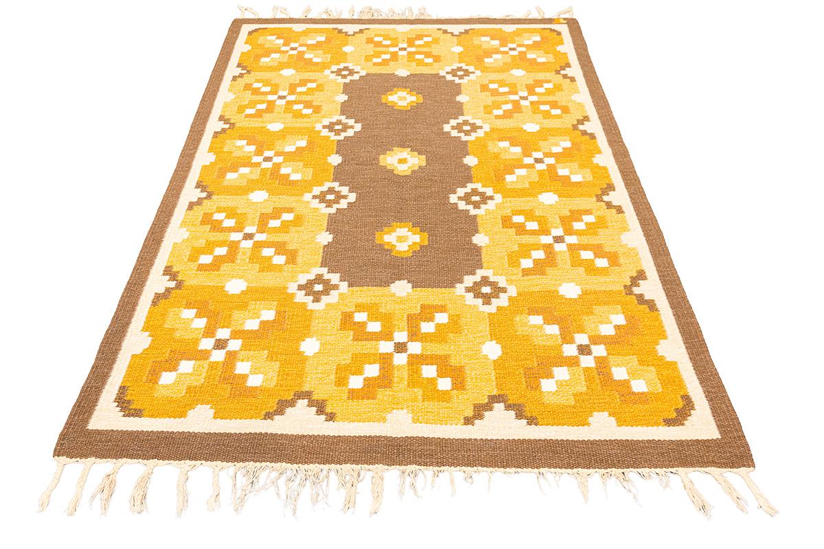 Tappeto scandinavo a trama piatta  Design Geometrico  Toni dorati
Questo splendido tappeto scandinavo a trama piatta presenta un audace disegno floreale geometrico disposto in una griglia simmetrica. La composizione è caratterizzata da marroni