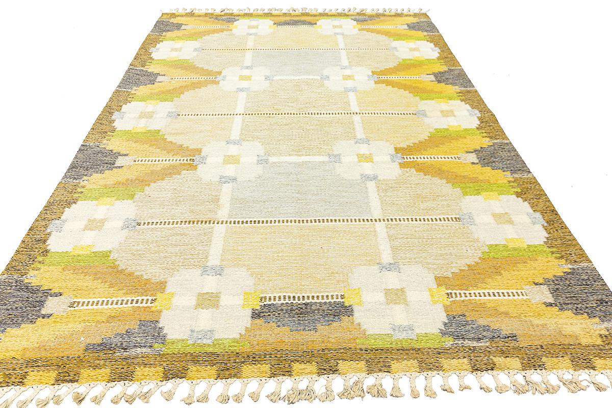This Scandinavian Rollakan rug, measuring 166 x 235 cm, is a beautifully woven flat-weave masterpiece, signed by the artist IS. The design embodies traditional Scandinavian aesthetics, featuring soft earthy tones of beige, mustard yellow, olive