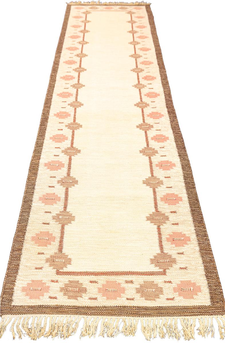 Be prepared to be captivated by the beautiful Swedish Rollakan Rug! This eye-catching piece combines simple design with a flat weaving technique, creating an interesting and unique texture. Its delicate and inviting pinkish hue is brought to life