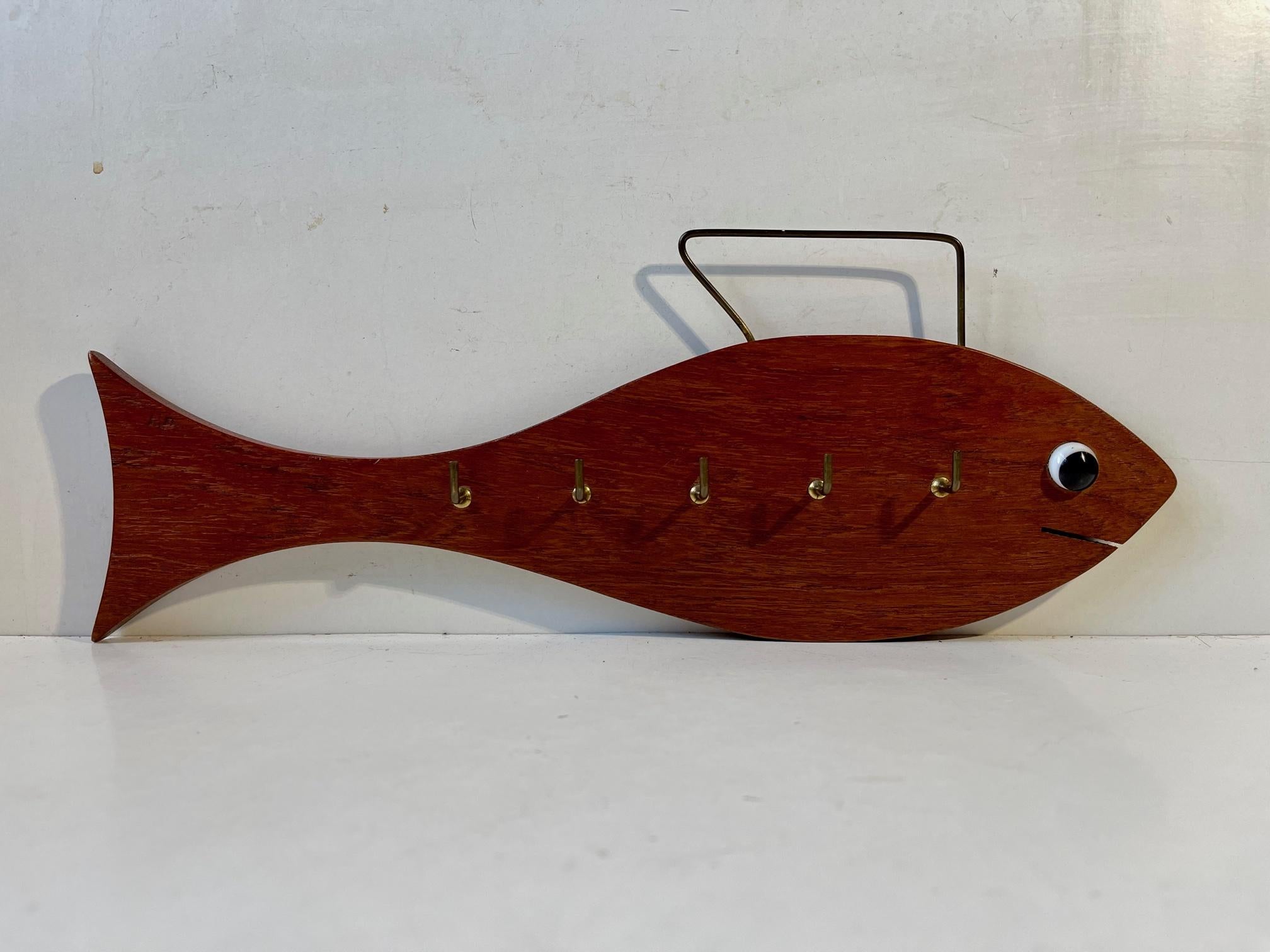 Unusual wall mounted shark-shaped key holder in teak. Decorated with details in brass and a black and white glass eye. Imprinted to its backside HAJ, Copyright. Possibly designed by Hans Agne Jakobsson who frequently marked his designs HAJ.