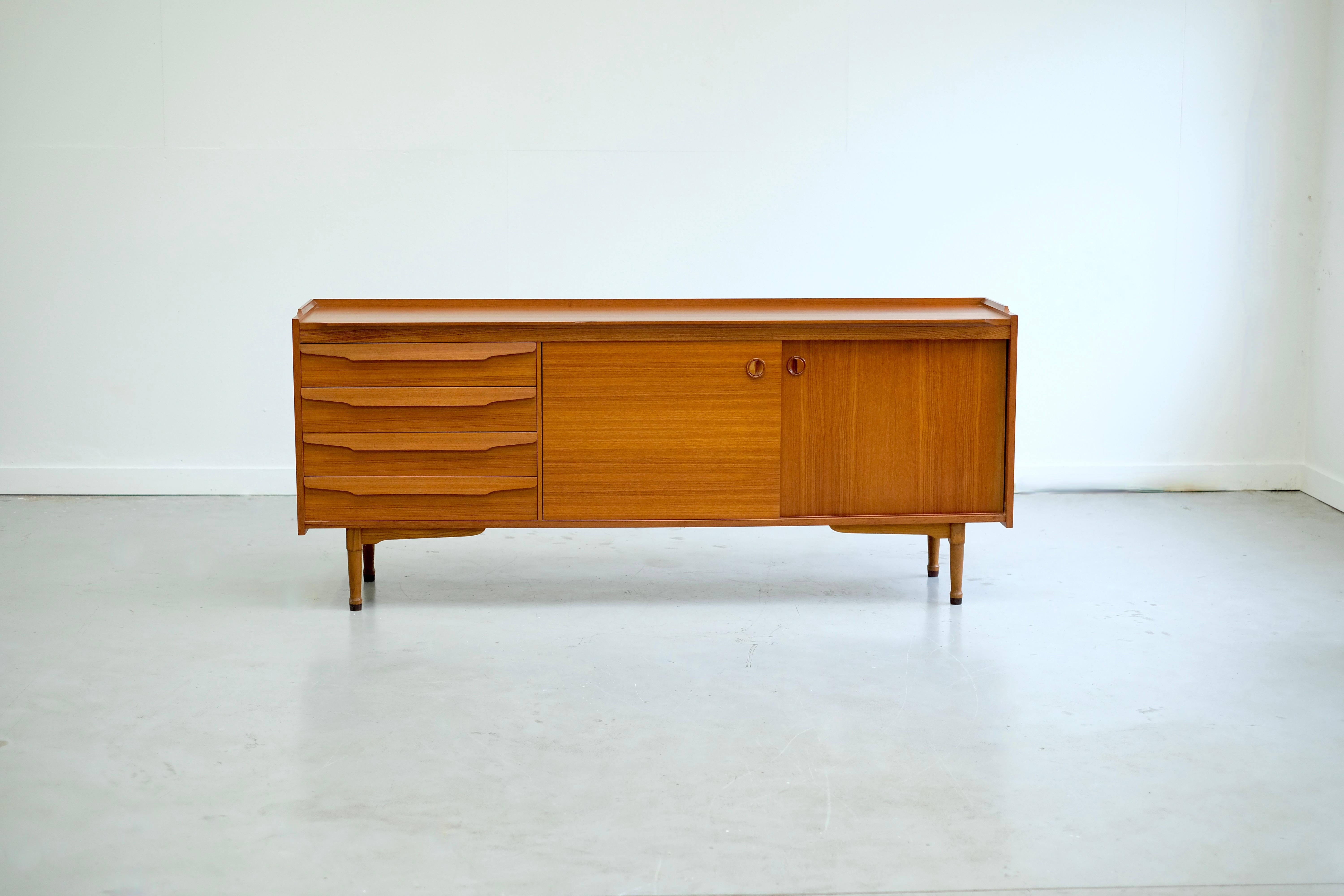 Magnificent Scandinavian teak sideboard designed in the 1960s.
It has 2 sliding doors housing 2 storage spaces.
On the left side of the sideboard there are 4 very spacious drawers.

We can admire very beautiful borders on the top of the sideboard