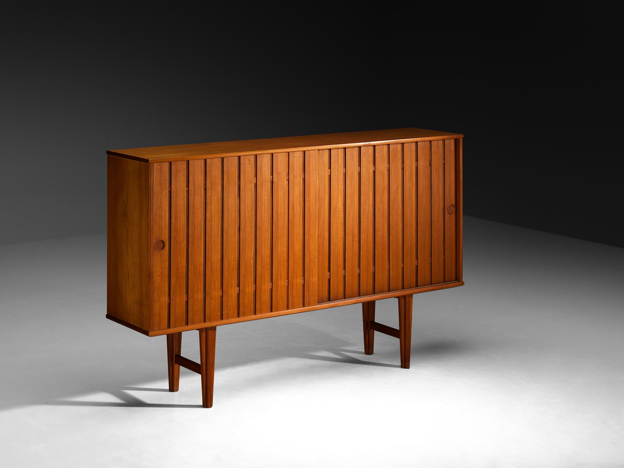 Sideboard, teak, Scandinavia, 1960s

This very elegant and slender sideboard is made in the 1960s in Scandinavia. The two slatted sliding doors in front both have a recessed handle, keeping a clean aesthetic. The interior offers plenty of storage