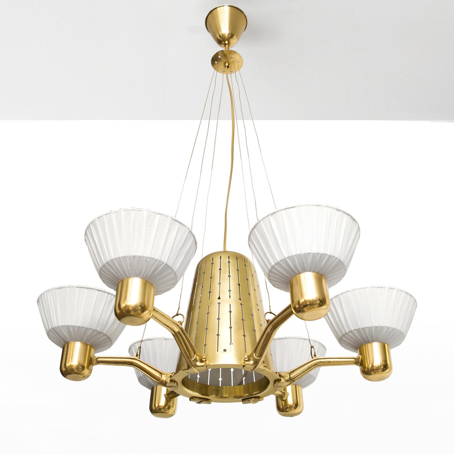 Hans Bergstrom, Scandinavian Modern six-arm chandelier in polished brass with newly restored fabric shades. The fixture’s dome centre form is detailed with a pierced vertical pattern. A single socket and bulb illuminate the centre domed body. Newly