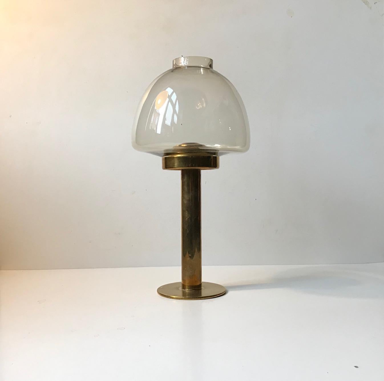 This candleholder Model L102/32 features a mouth-blown smoked hurricane glass shade and a brass base with a spring mechanism that pushes the candle upwards while burning. It was designed by Hans Agne Jakobsson and manufactured by his company