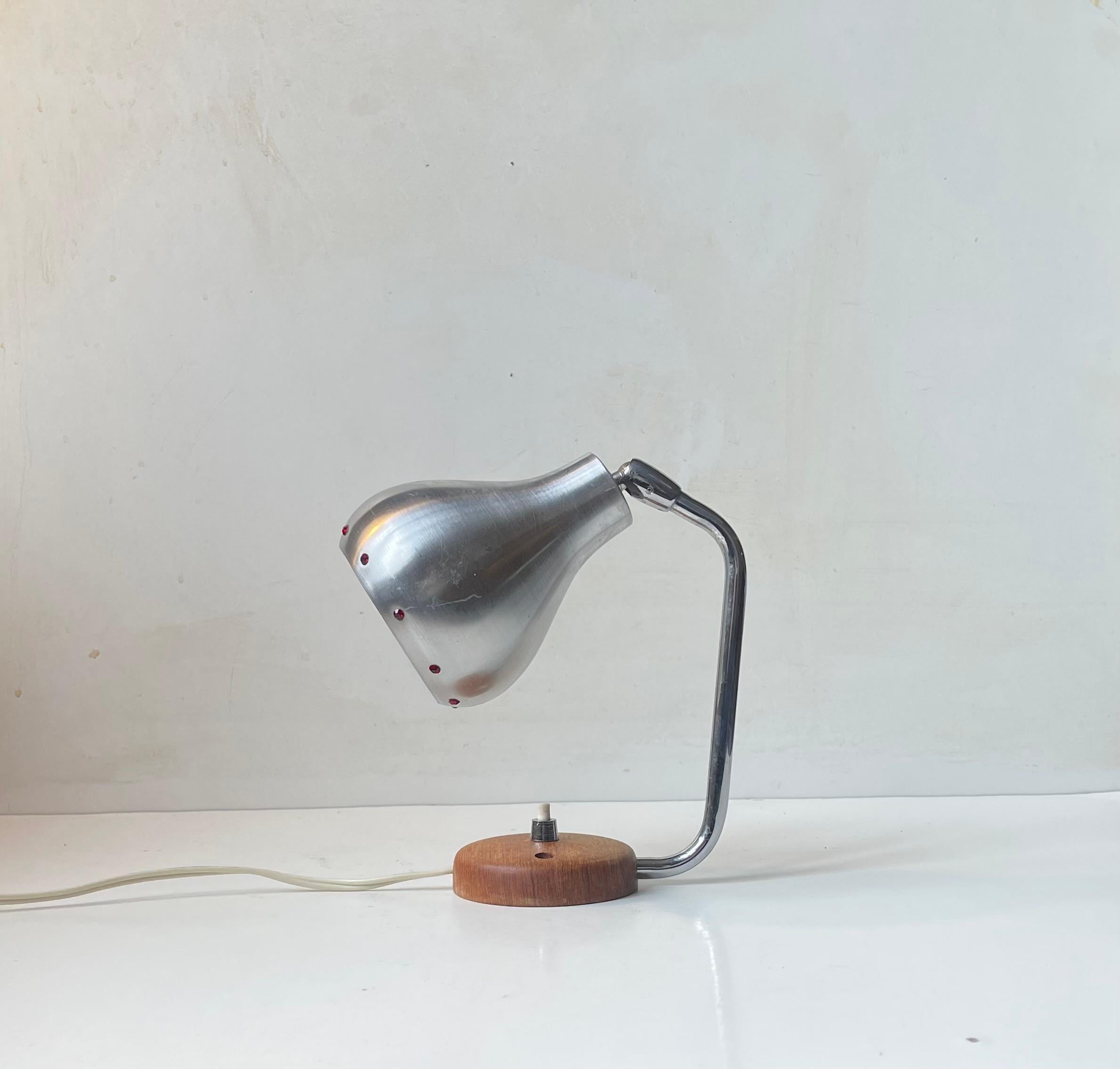 Interessante lampada da parete composta da una solida base in teak con interruttore on/off, un braccio regolabile e un paralume in alluminio ingioiellato con finti rubini (acrilici). Probabilmente prodotto da Vitrika in Danimarca o da Ewå Värnamo in