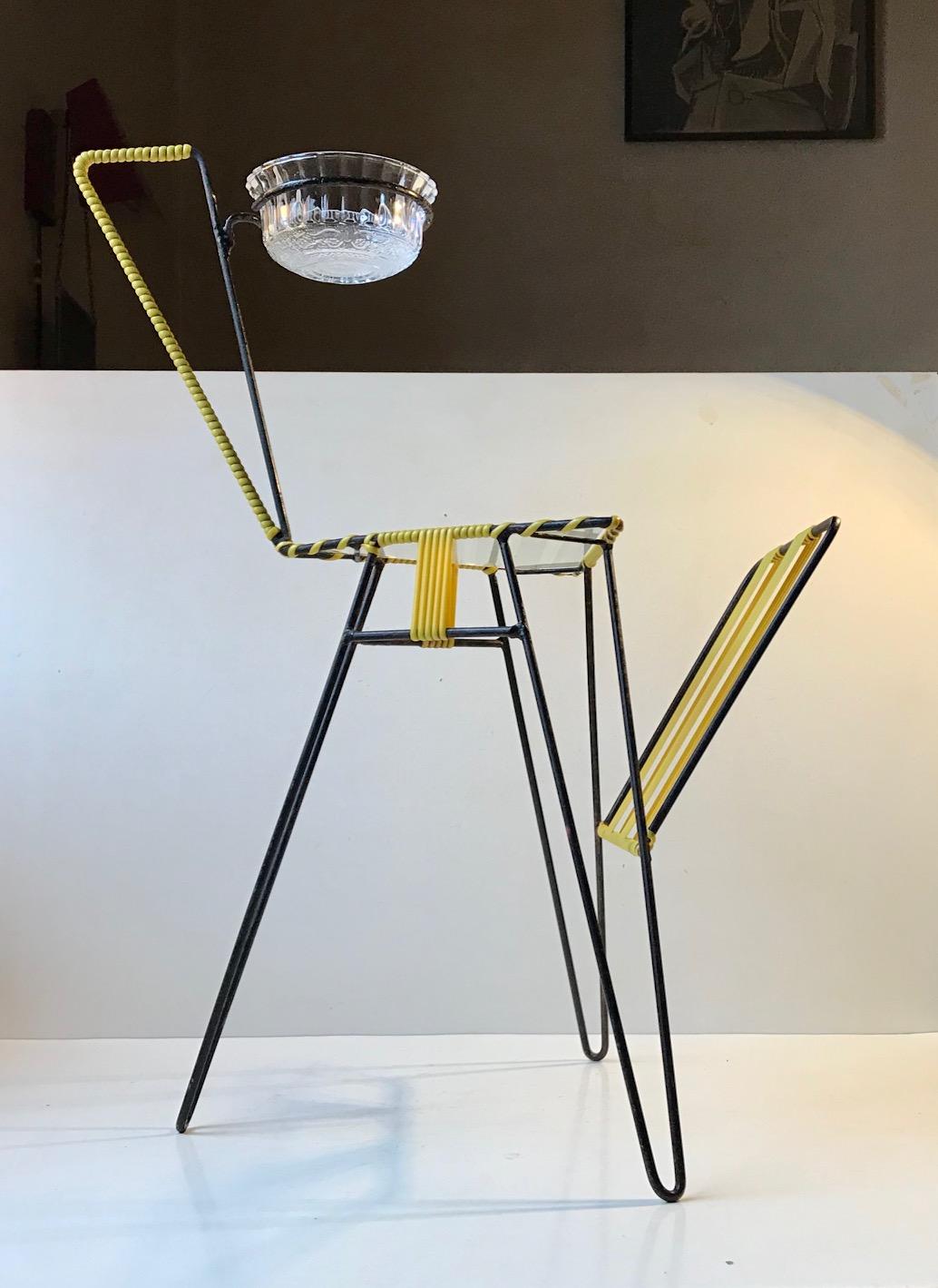 A graphic looking magazine rack with a removable bowl or ashtray. Its is commonly called the Giraffe due to its shape. The body is constructed from bend wire/string iron painted in black and with yellow acrylic cane details.