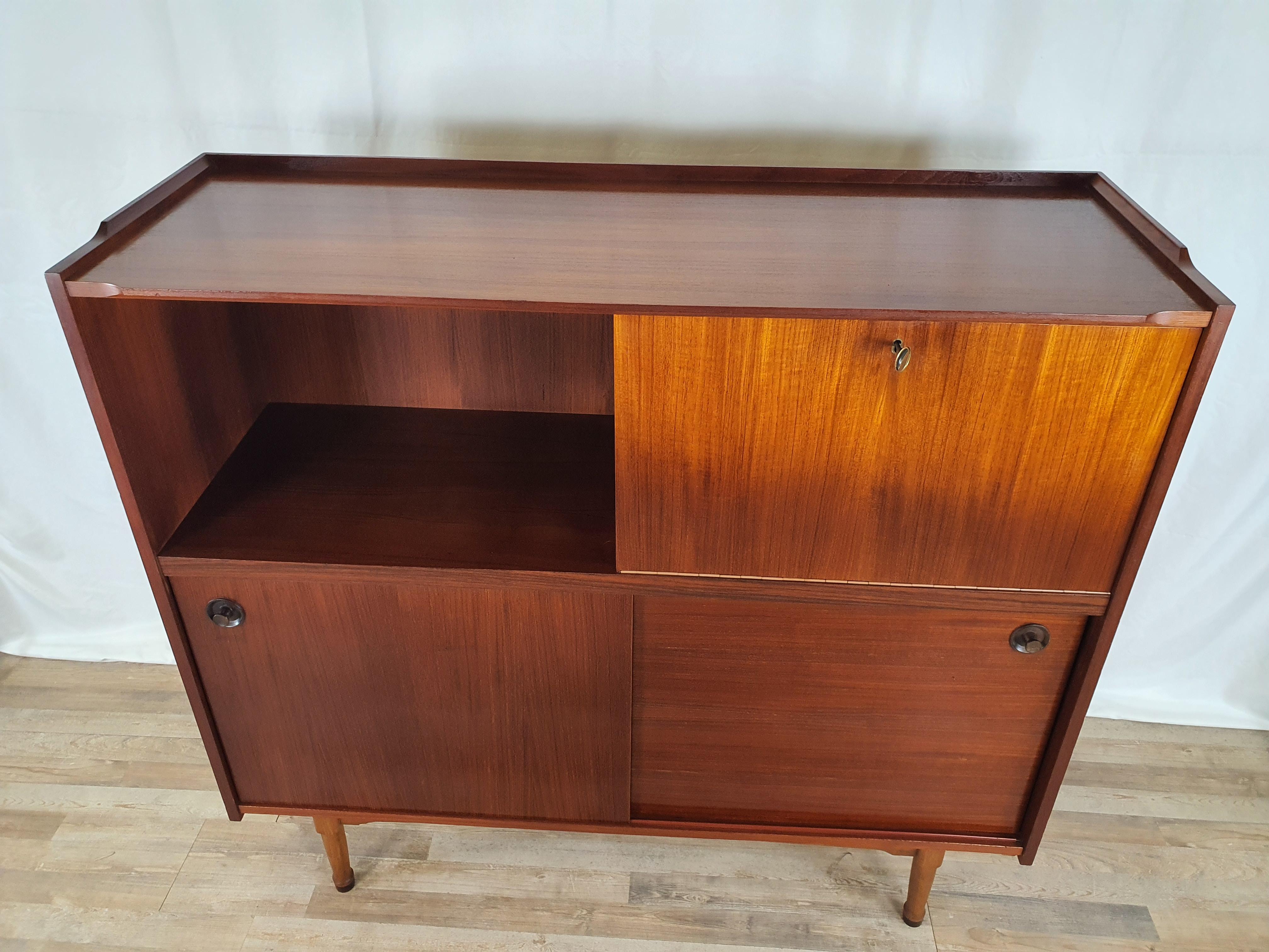 Scandinavian style sideboard entirely veneered in teak with double sliding and flap doors.

Open space on the left side and flap with brass key on the right side, inside there is a colored and worked glass top and a small transparent glass