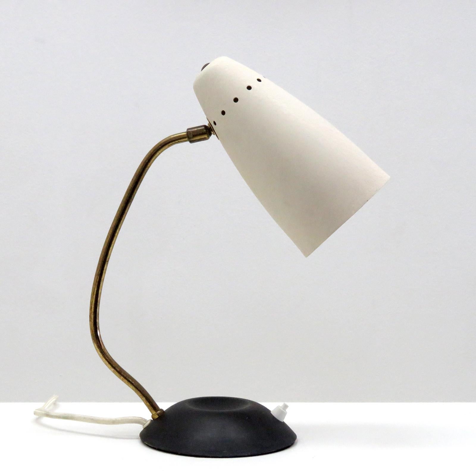 Elegant articulate table lamp, with matte black metal base, curved brass arm, orientable aluminium shade in textured ivory, on/off switch on the base, wired for US standards, one E27 socket, max. wattage 75W, bulbs provided as a one time courtesy.