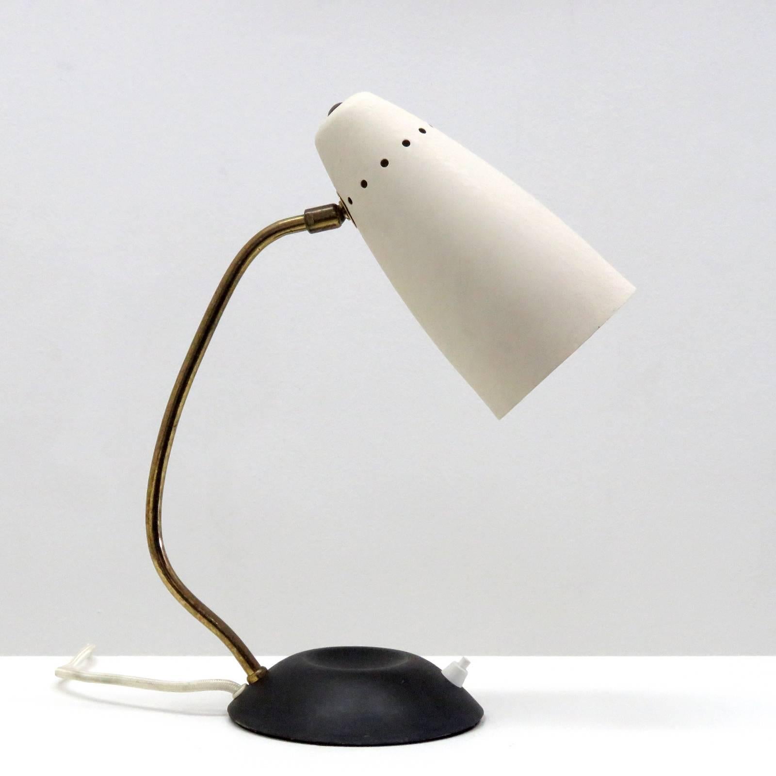 Elegant articulate table lamp, with matte black metal base, curved brass arm, orientable aluminium shade in textured ivory, on/off switch on the base.