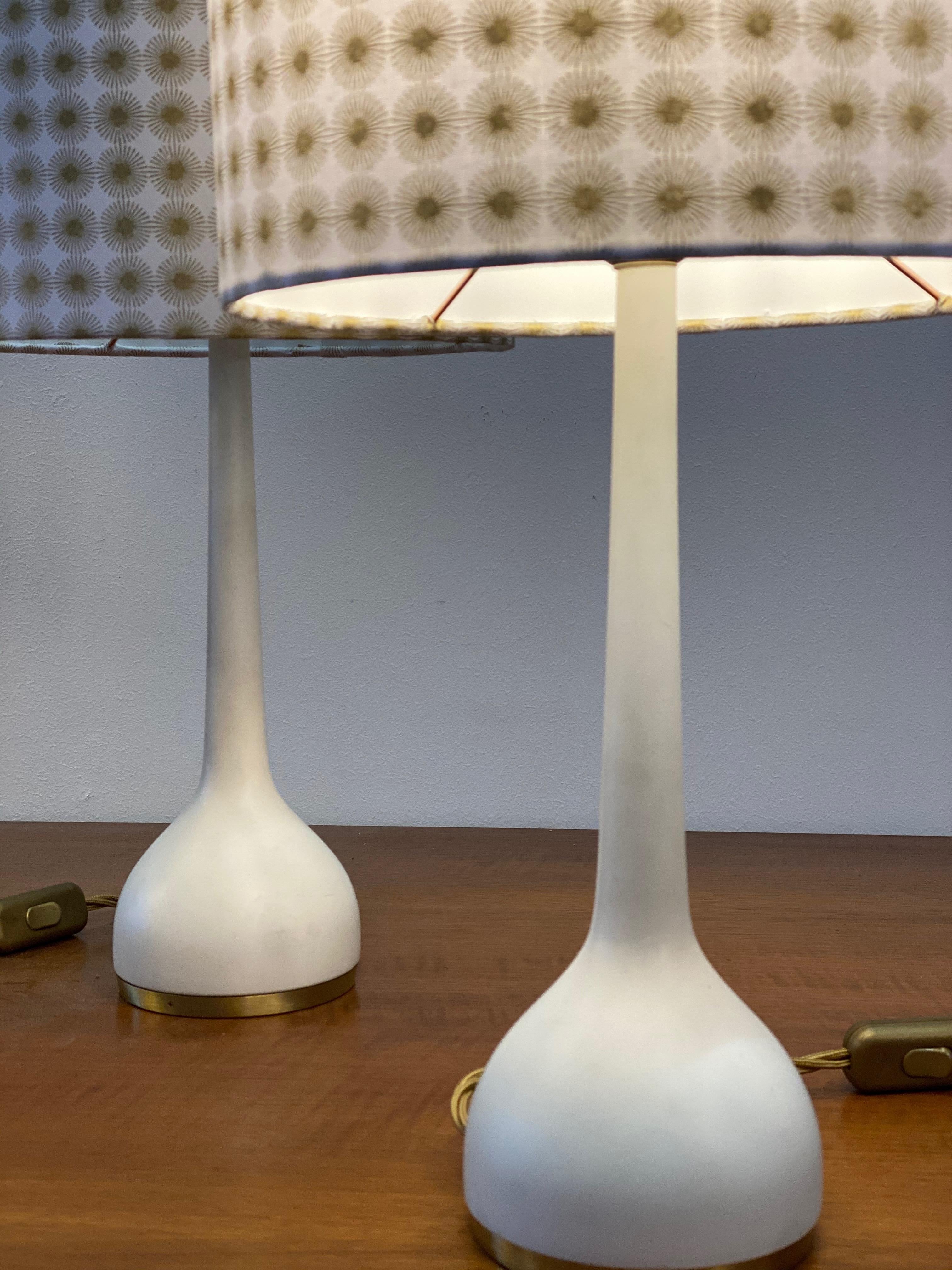 These table lamps were designed by Hans-Agne Jakobsson in the 1960s and manufactured by Hans Agne Jakobsson AB in Markaryd, Sweden. It comprises a white lacquered base with original fabric shades. The bas as well as the shades are marked with the
