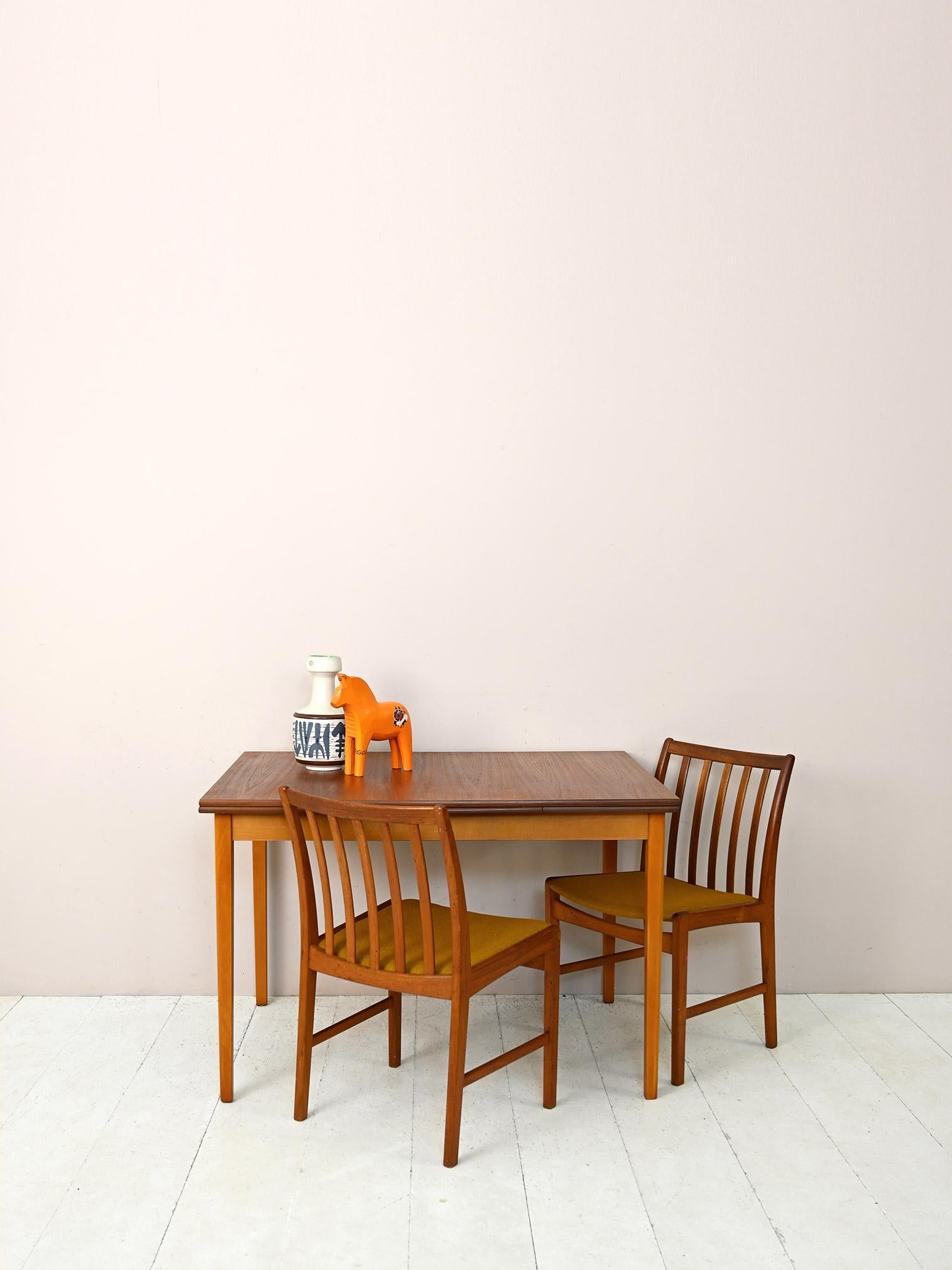 1960s dining table with teak top.

This modern and functional piece of furniture is characterized by the fact that it can be extended thanks to the pull-out planks located on the two short sides.
The deep color and pronounced teak wood grain of the